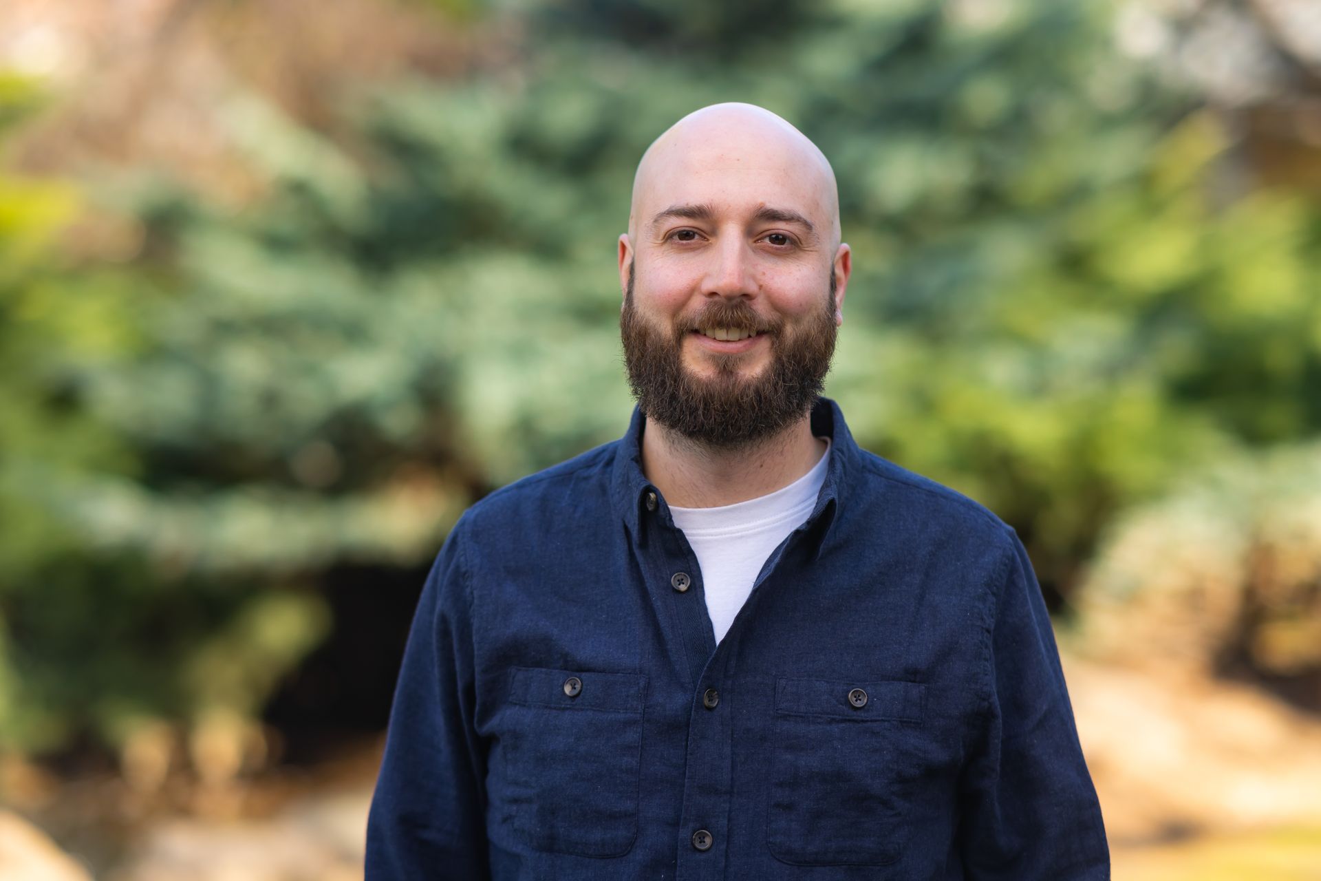 A bald man with a beard is wearing a blue shirt and smiling for the camera.