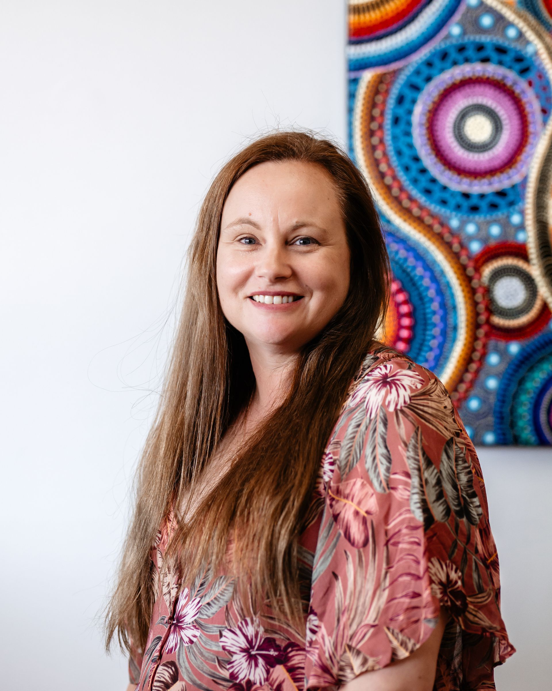 A woman wearing glasses and a necklace is standing in front of a white wall.