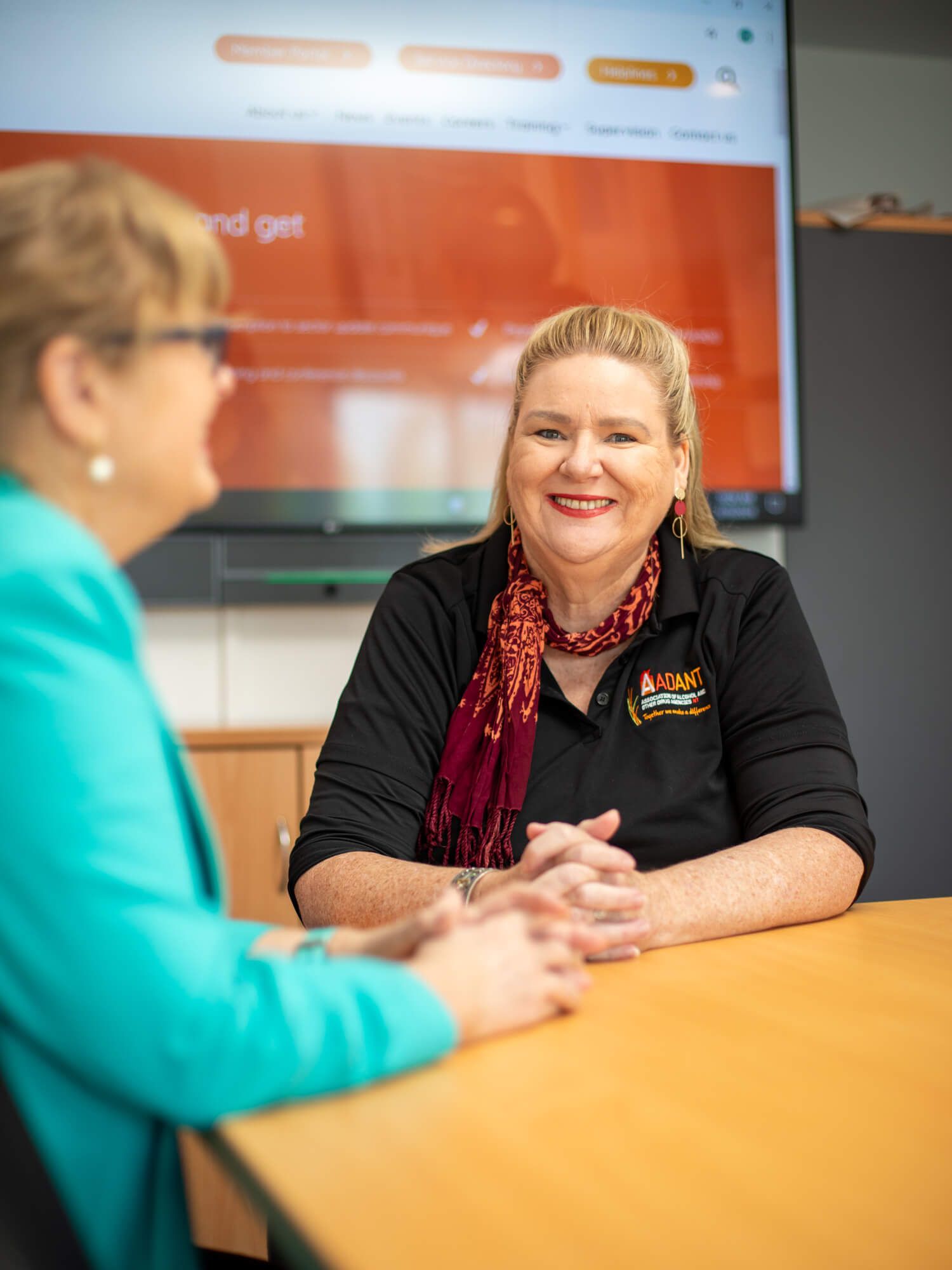 Two women are sitting at a table talking to each other.