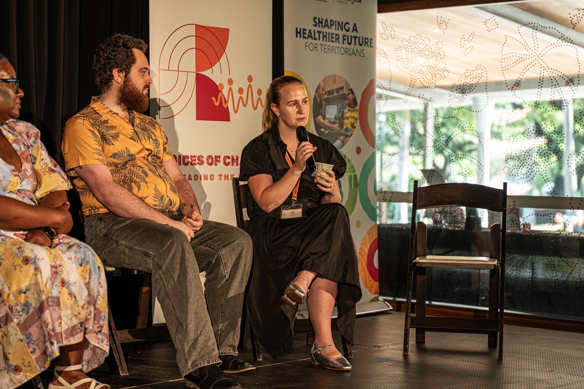 Three people sit on a stage during a panel discussion, with the person in the middle speaking into a handheld microphone.