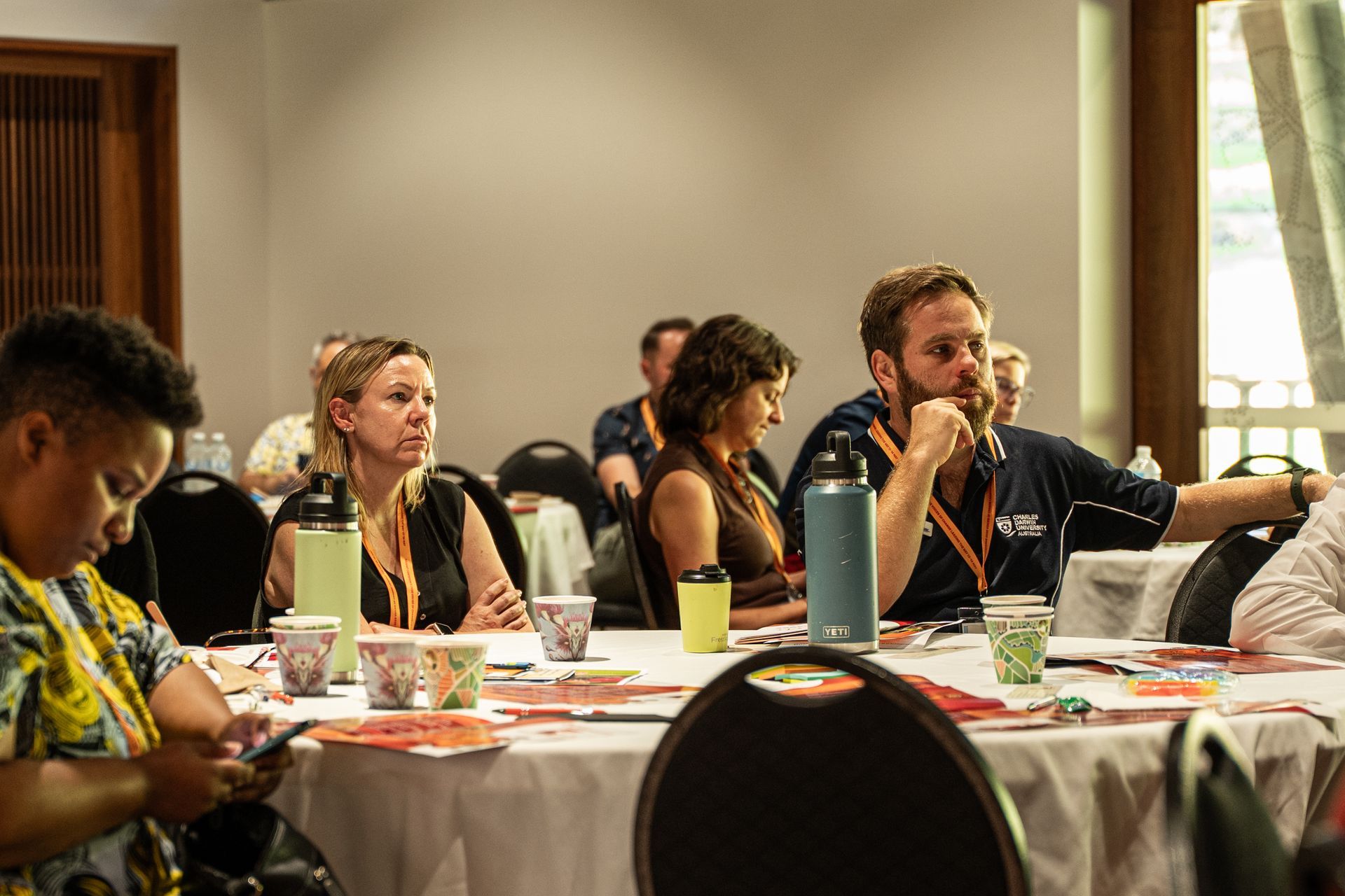 Attendees listen attentively during a professional workshop in a well-lit conference room with round tables.