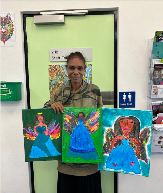 A woman is holding three paintings of angels in front of a green door