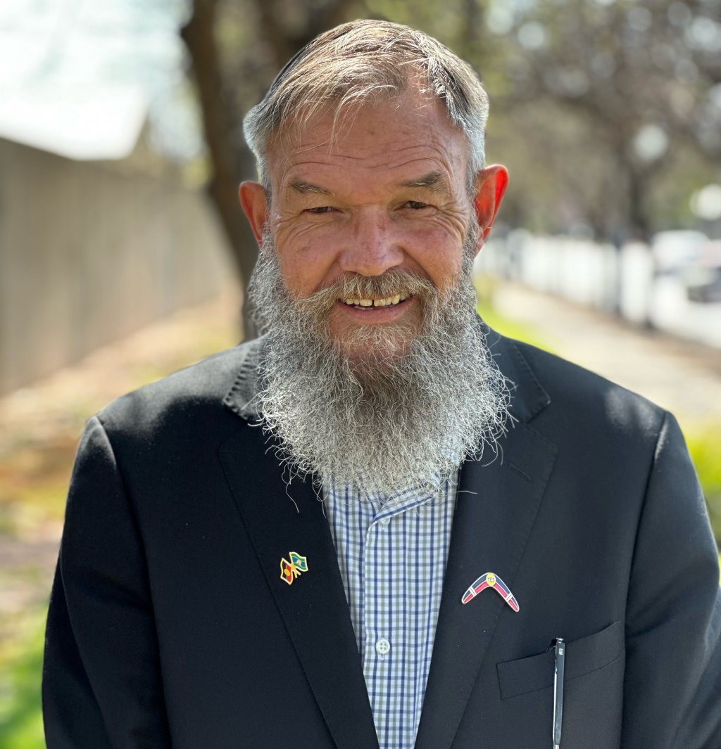 A bald man with a beard is wearing a blue shirt and smiling for the camera.