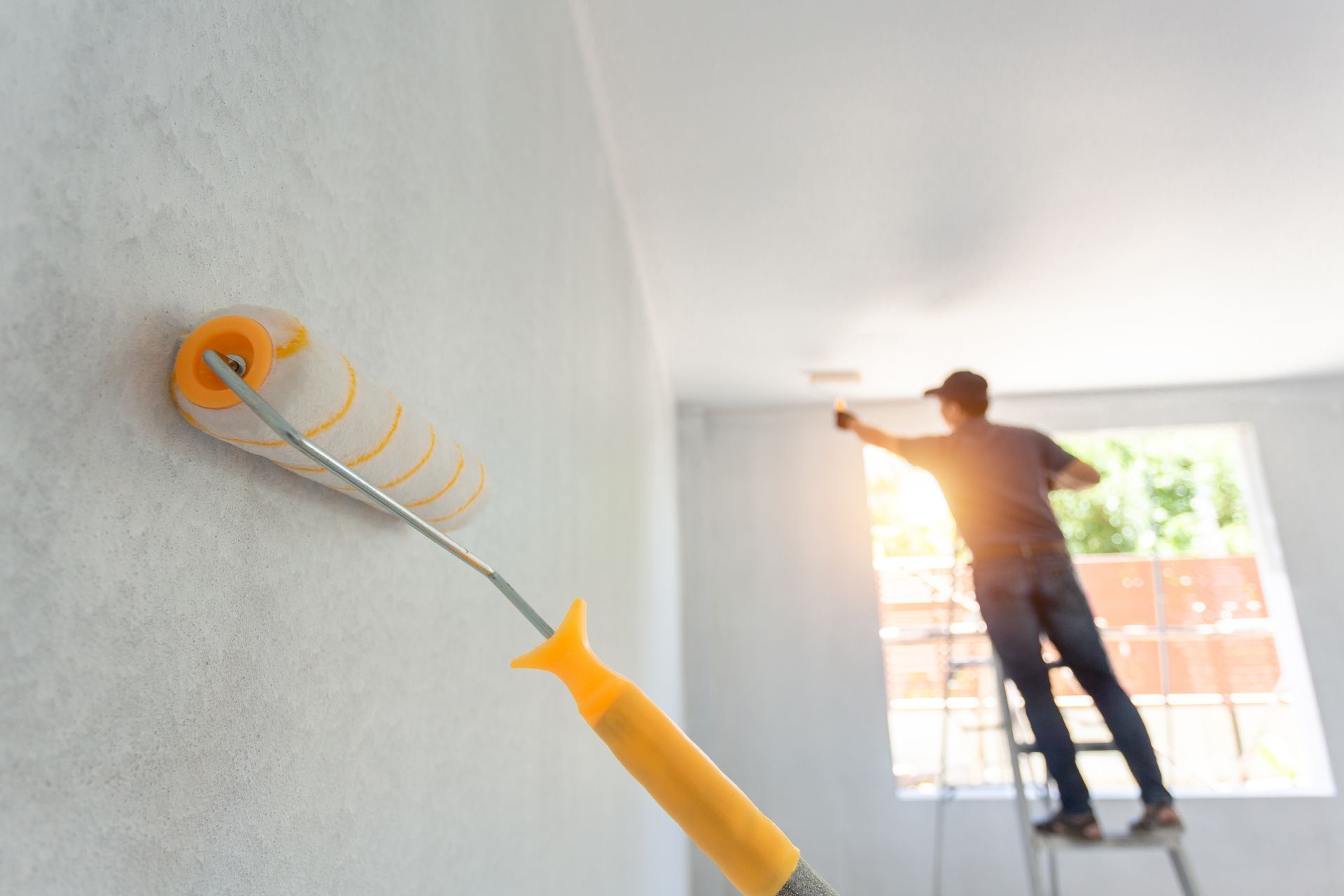a man on a ladder paints a wall with a paint roller