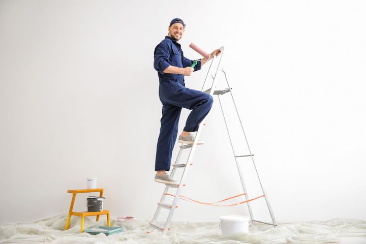 a man standing on a ladder holding a paint roller