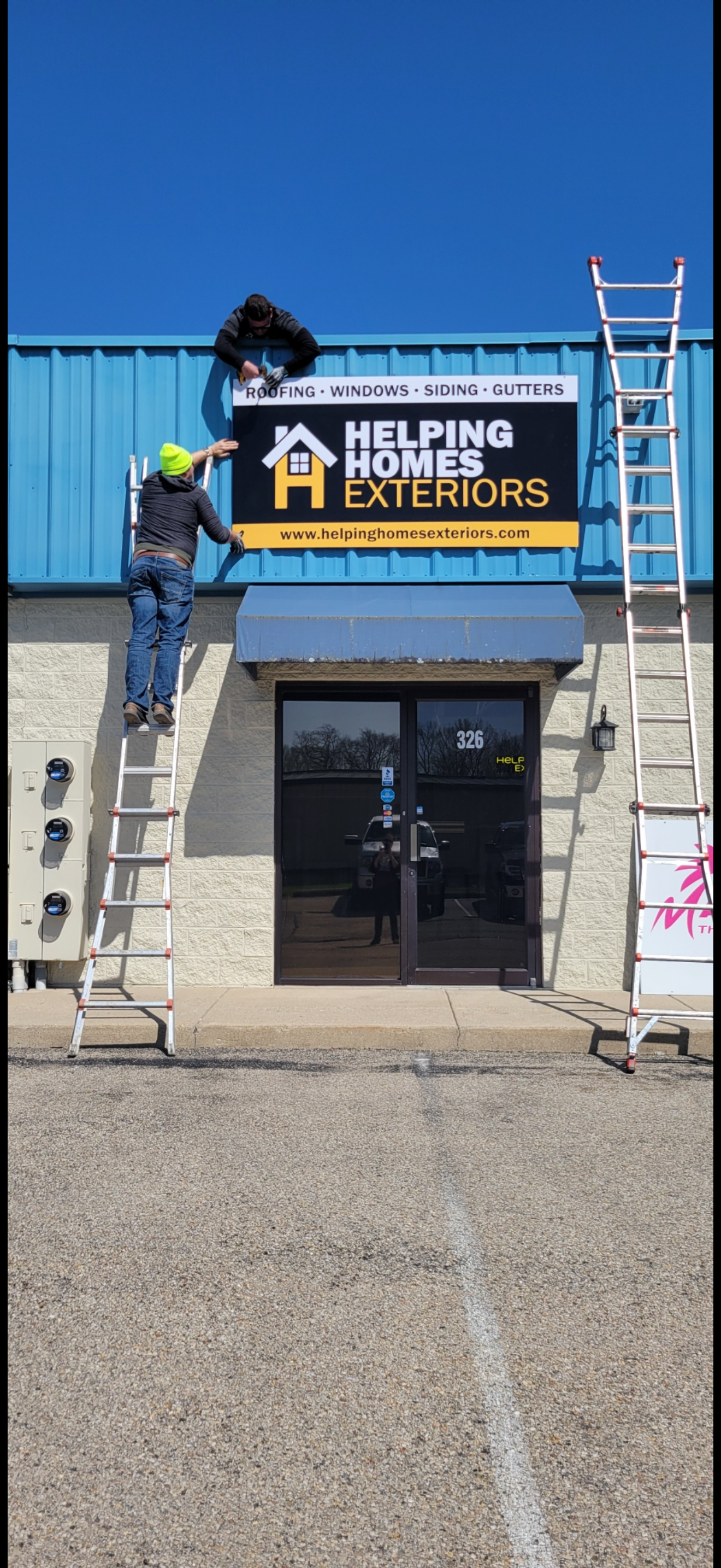 A person on a ladder is installing a sign that reads 