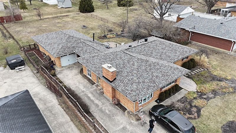 Overhead view of a brick house with a dark car parked in front of it on a concrete driveway.