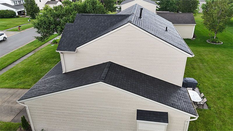 Two-story house with dark gray roof, light siding, and green lawn.
