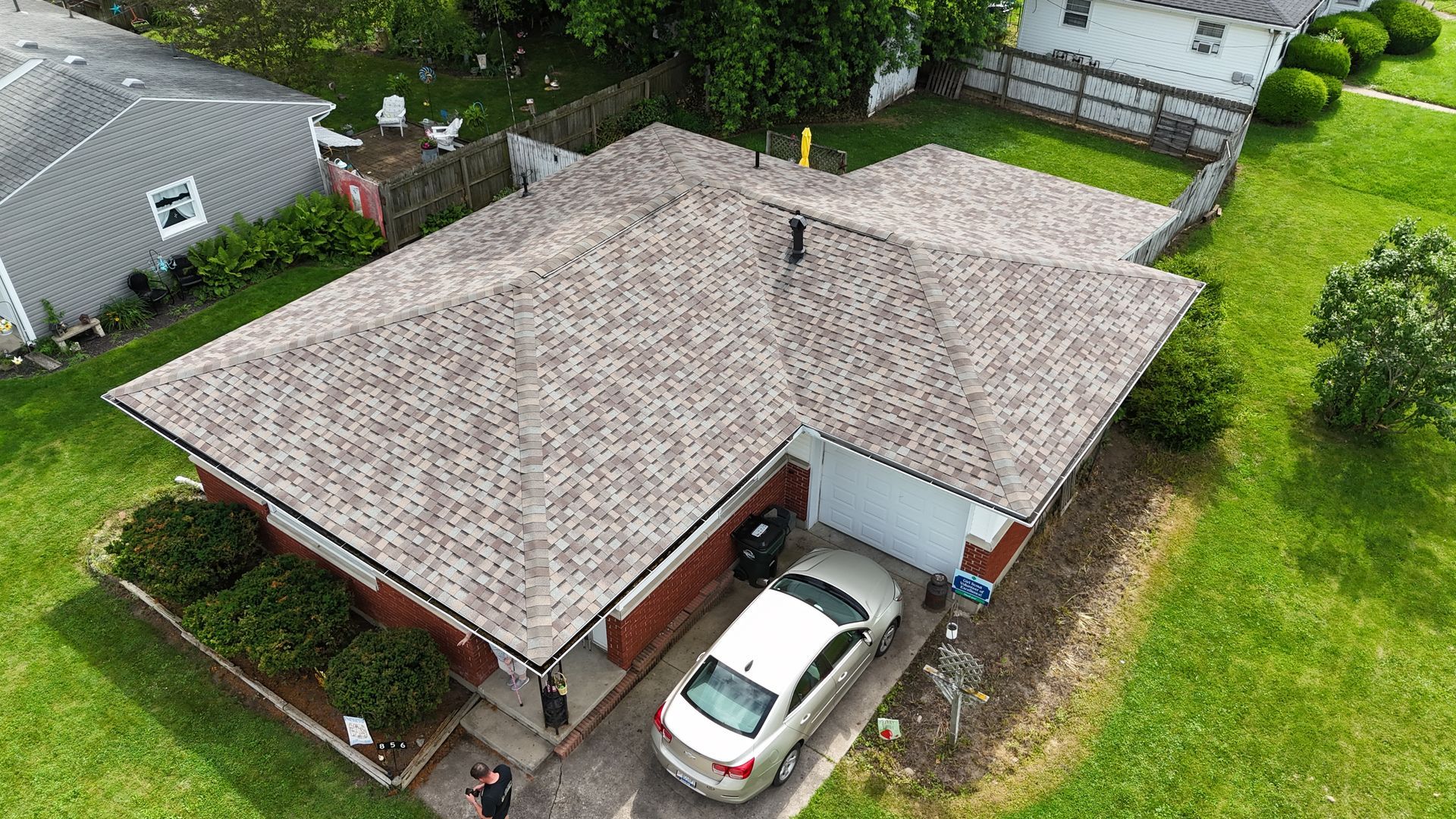 Aerial view of a suburban house with a car in the driveway and green lawn.