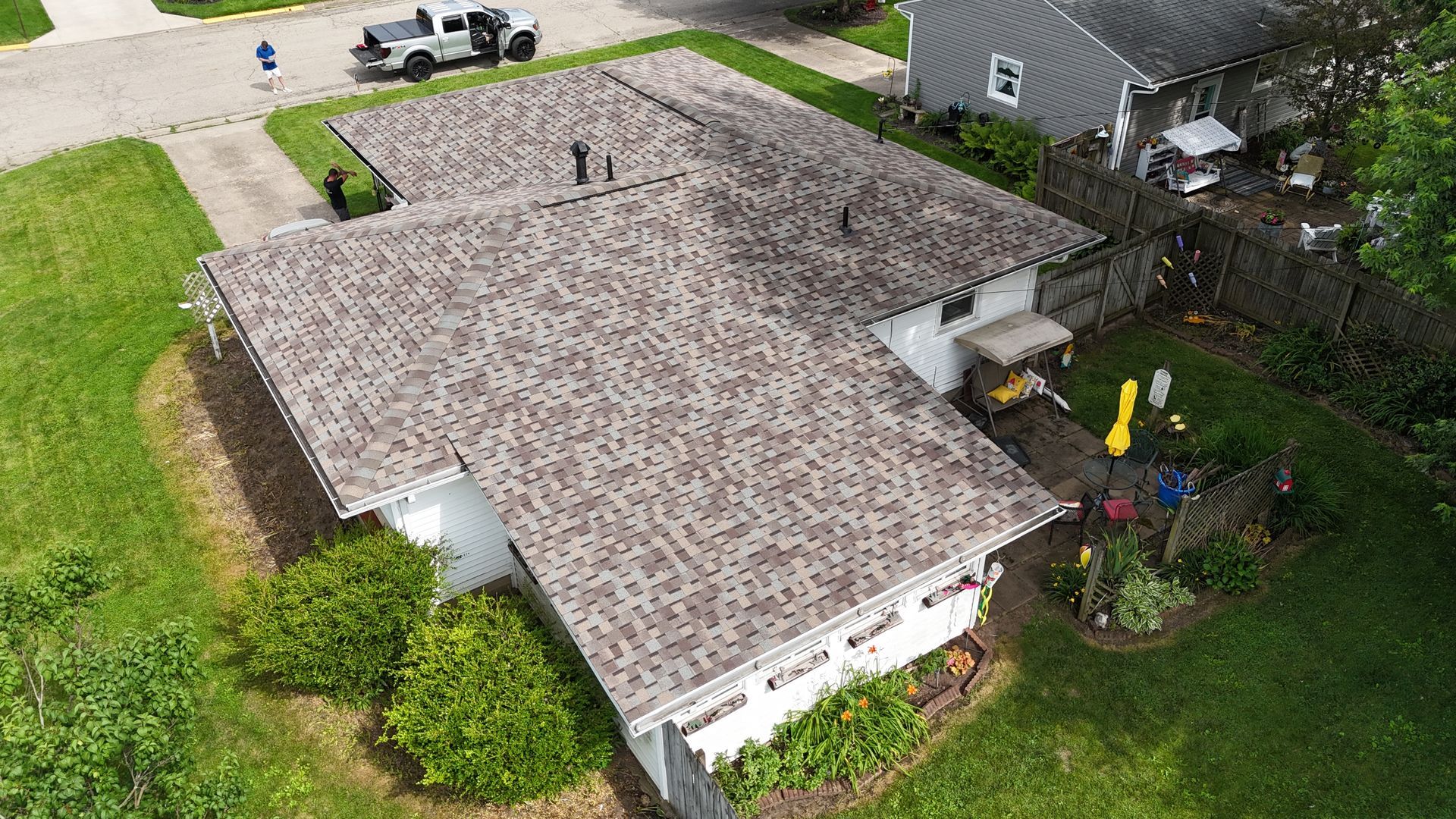 Overhead view of a house with a brown shingle roof, green lawn, driveway, and a white truck parked nearby.