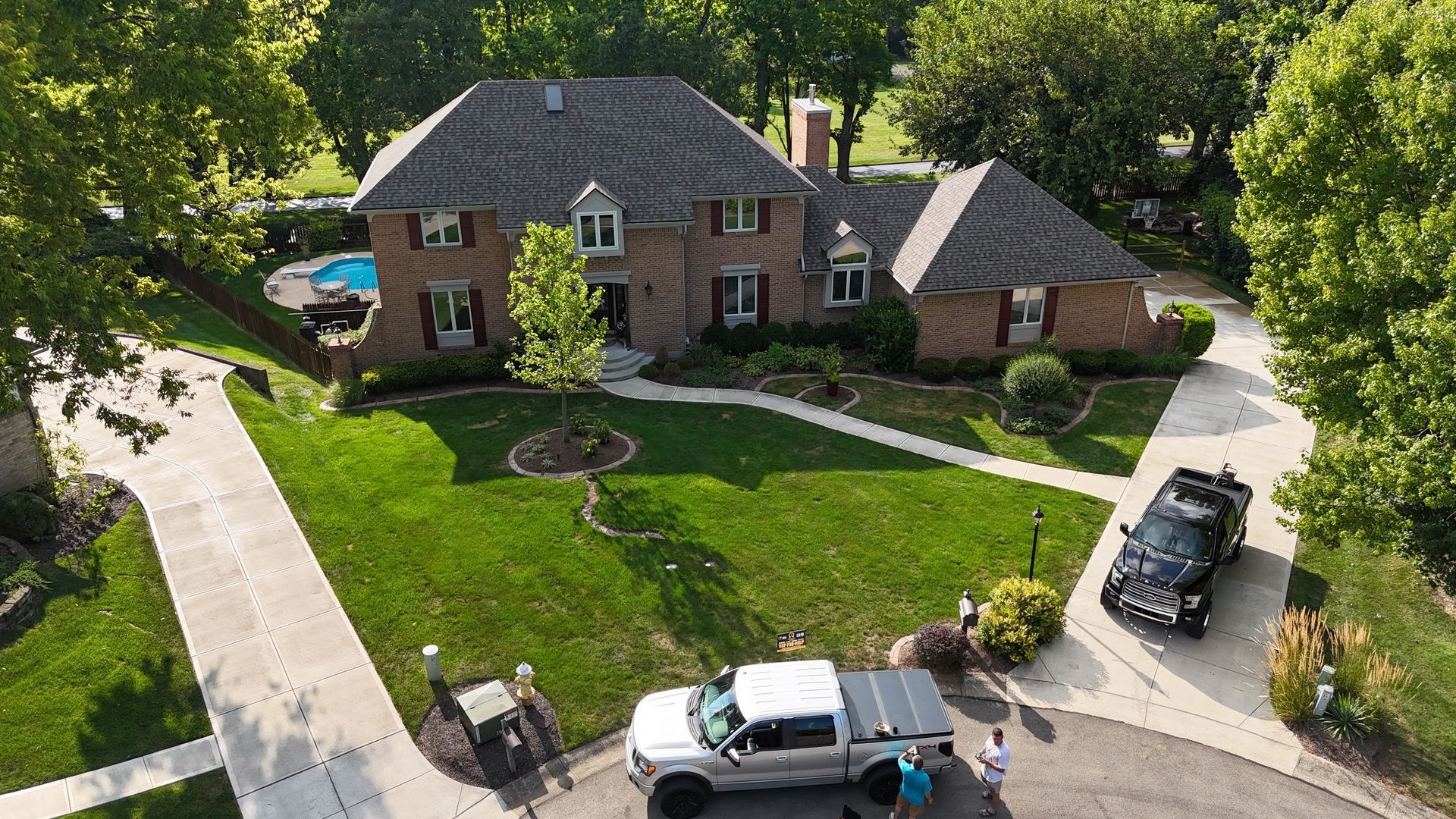 Brick house with green lawn, driveway, and parked truck and SUV. Trees surround the property.
