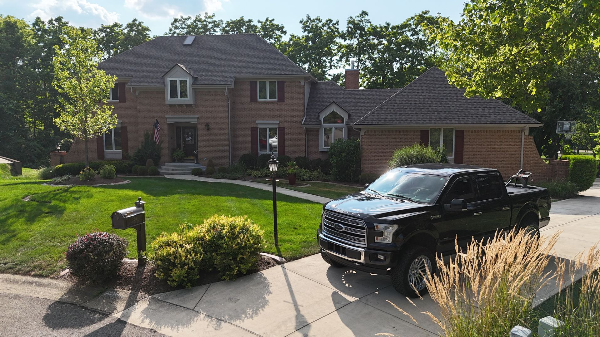 Black truck parked in driveway of a large brick house with green lawn.