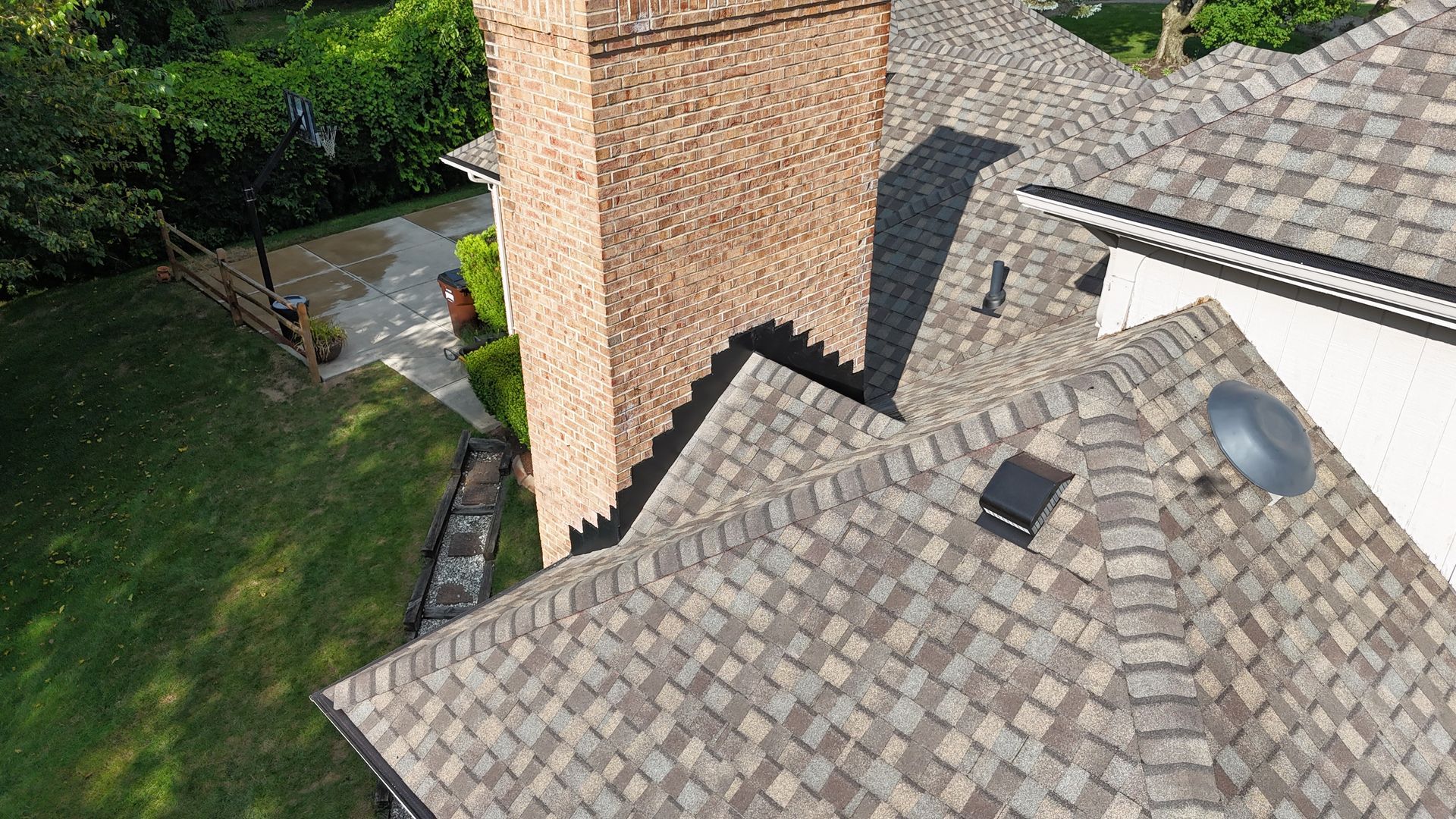 Roof of a house with brown shingles and a brick chimney, seen from above.