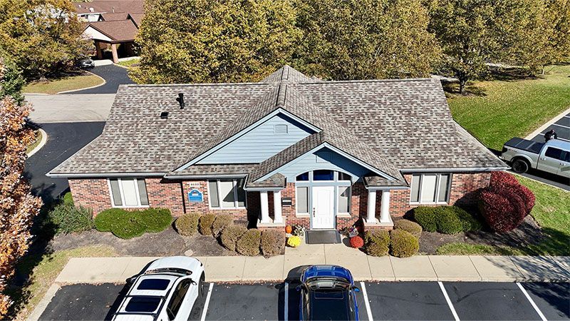 Brick building with brown roof and blue accents, parked cars in front.