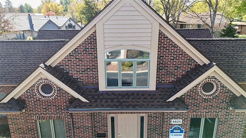Brick house with brown roof, arched window, and two round windows.