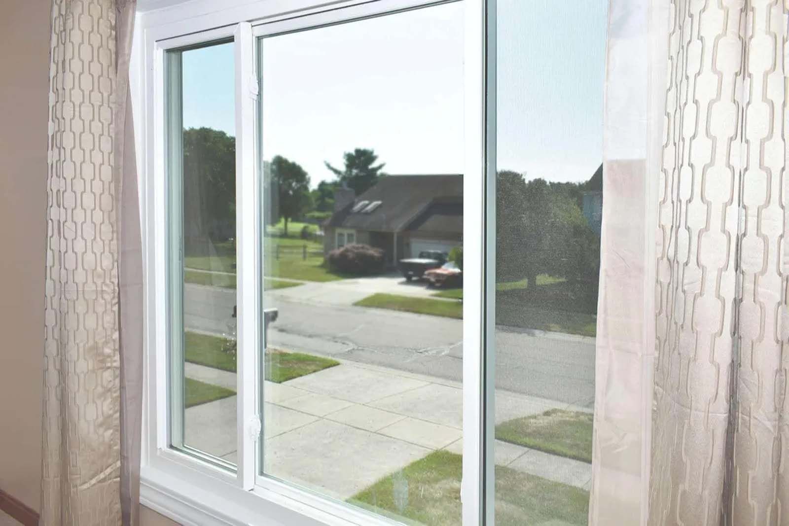 A sliding glass window with a view of a street and a house.