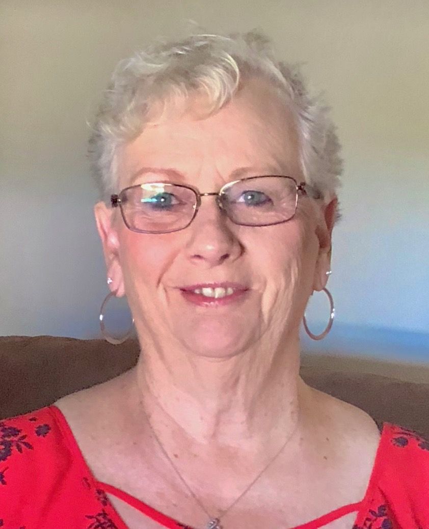 Woman with short gray hair, glasses, and hoop earrings smiles, wearing a red top.
