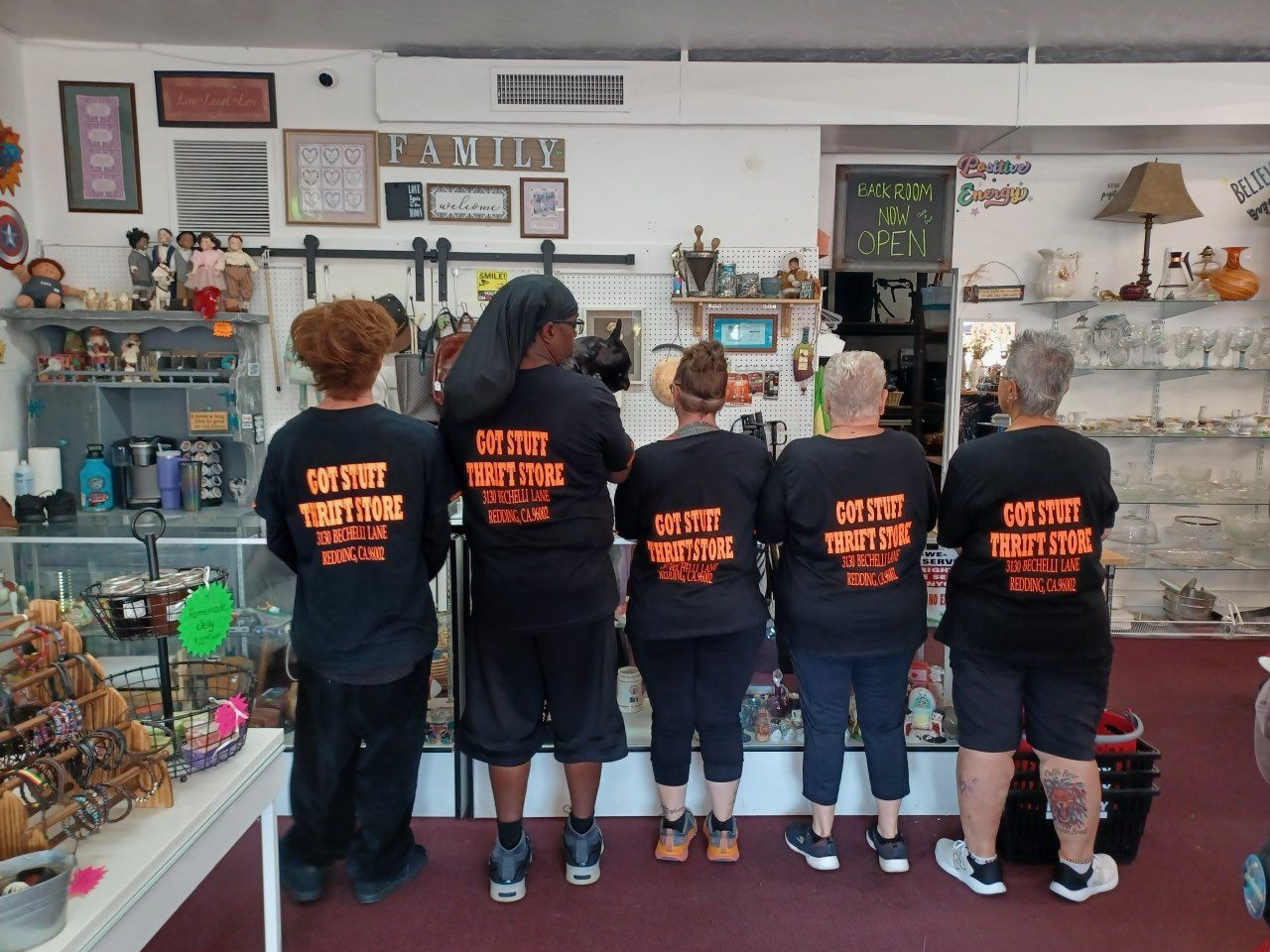 Five people in black shirts with text stand in a shop; backs to the camera.