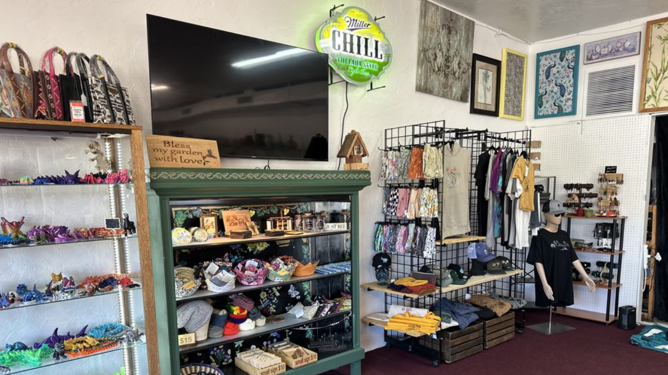 Inside a small boutique: colorful merchandise, clothing rack, artwork, neon sign, and display case.