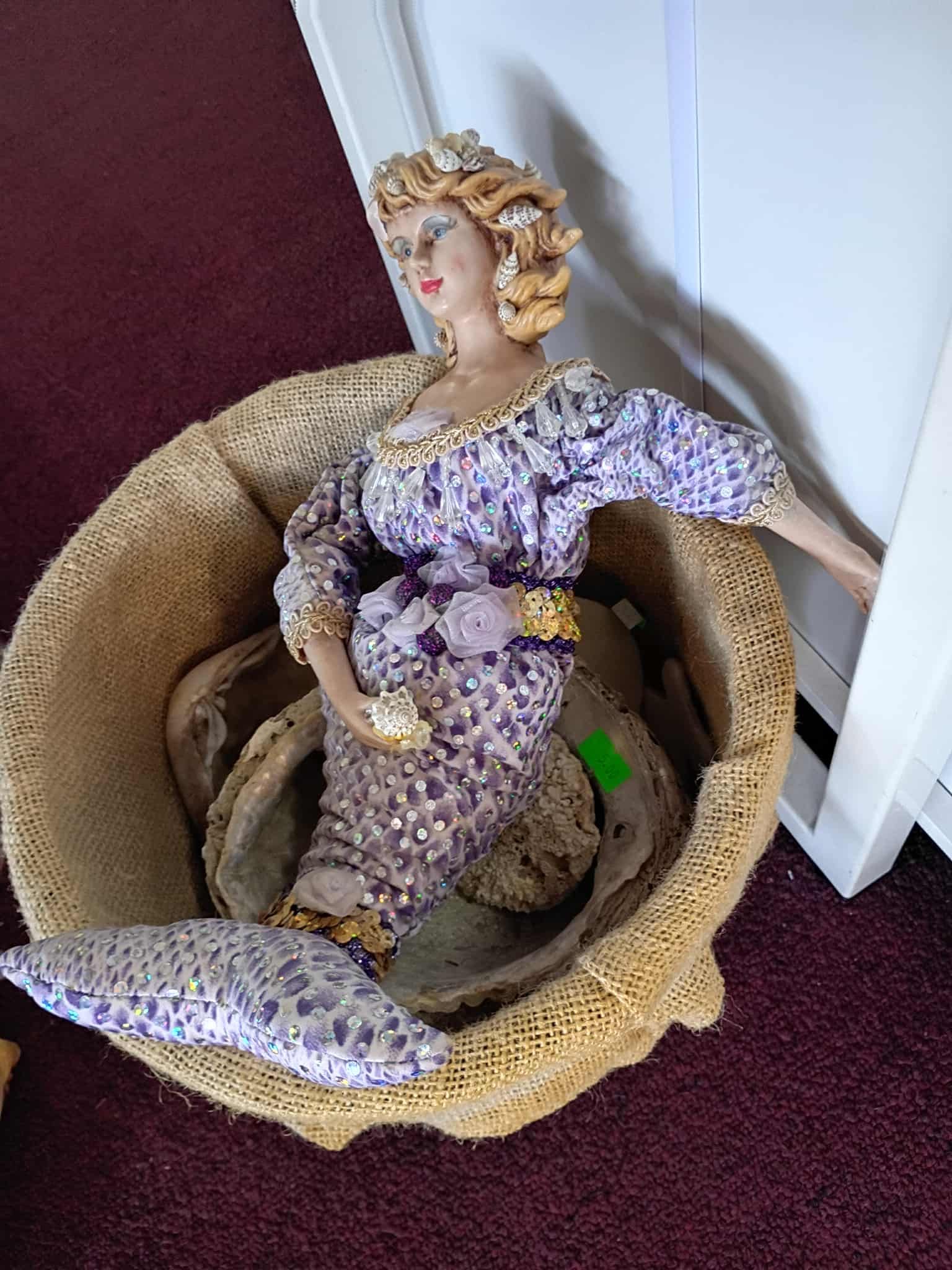 Woman figurine in purple gown in a woven basket, on a red surface.