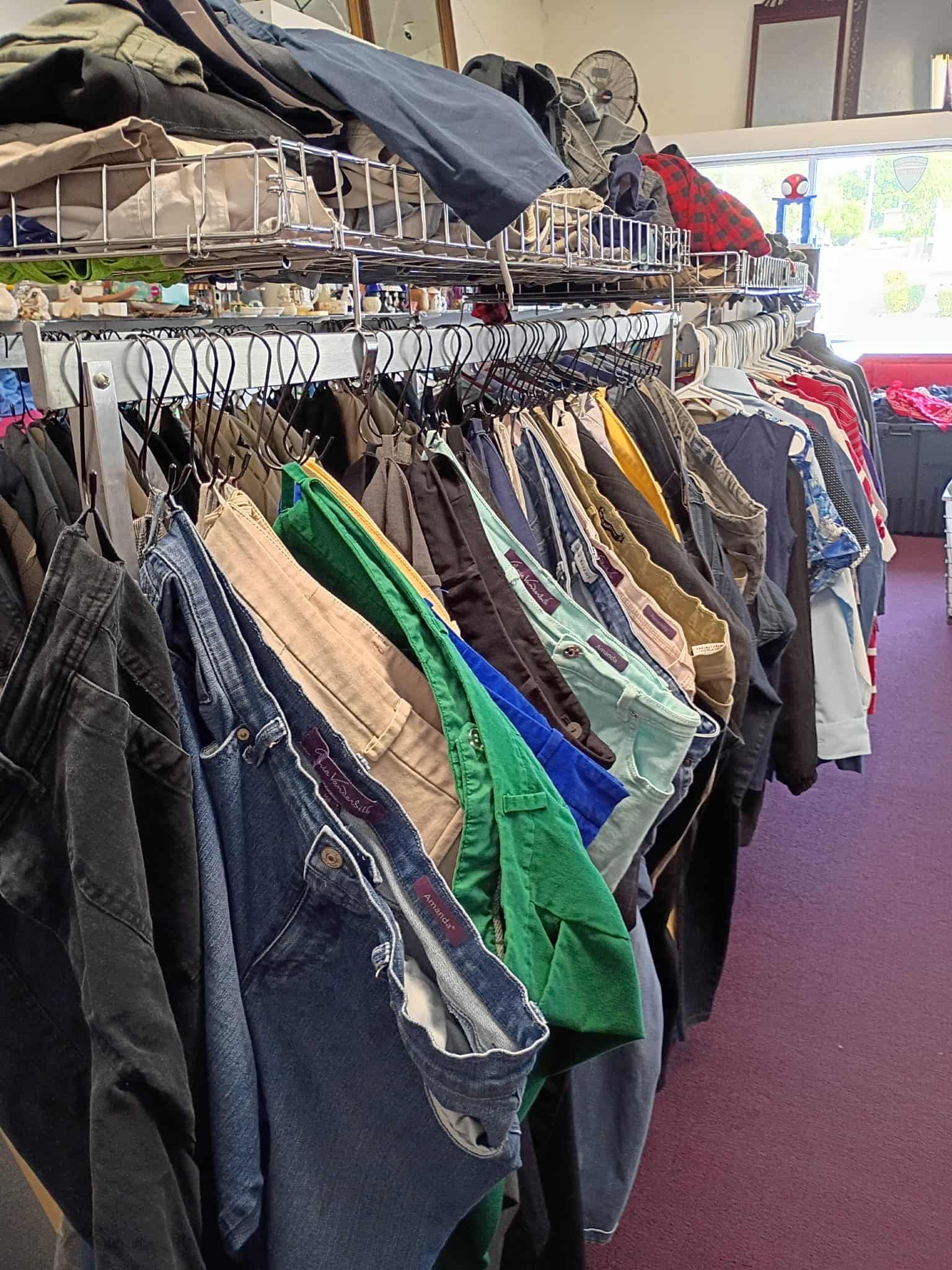 Clothes hanging on racks in a store, including jeans, shorts, and shirts of various colors.