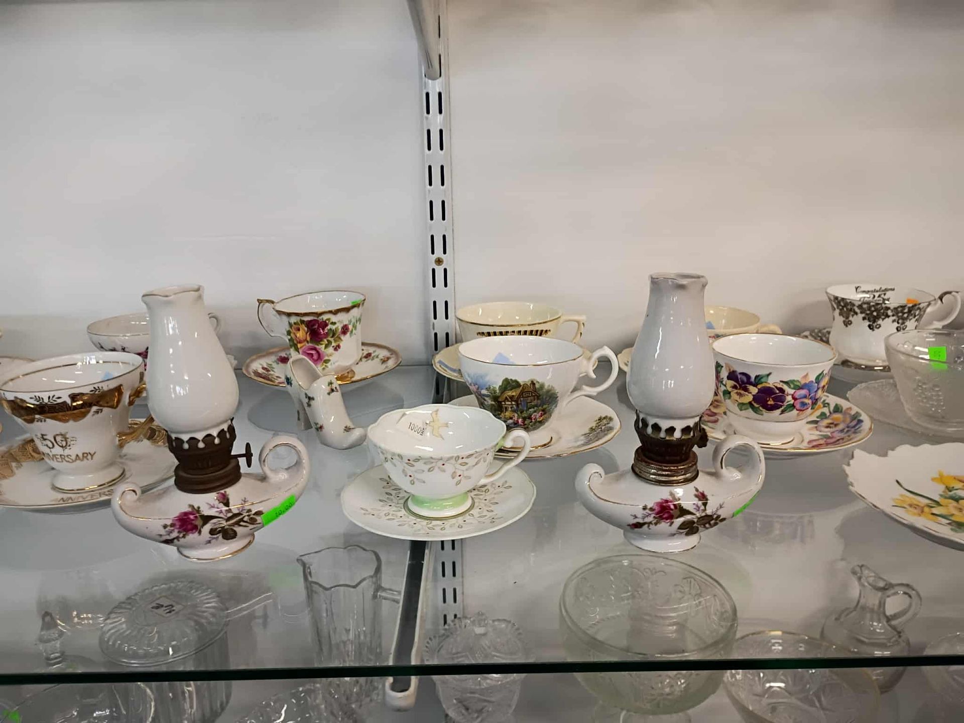 Teacups and saucers, some repurposed as oil lamps, displayed on shelves.