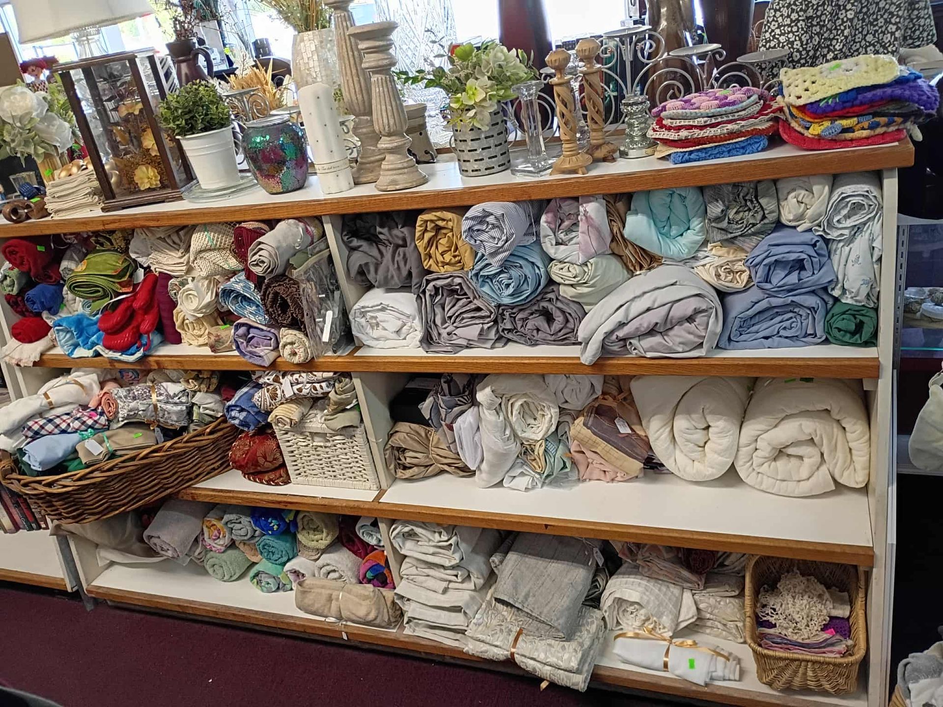 Shelves filled with folded fabrics, towels, and decorative items, in a store setting.