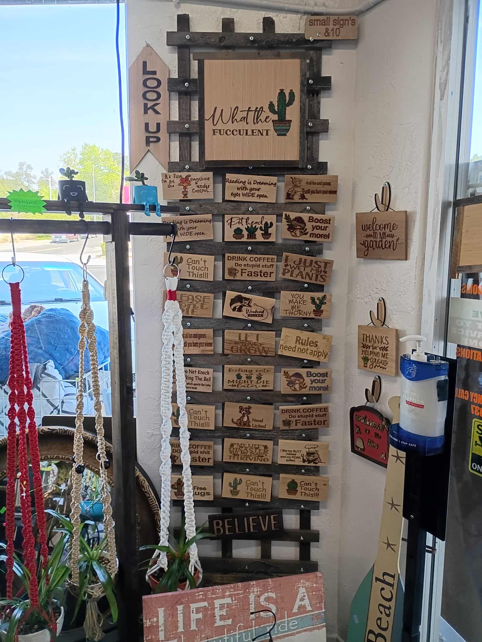 Wooden signs displayed on a trellis in a shop. Some signs have words/images. Other merchandise is visible in the foreground.