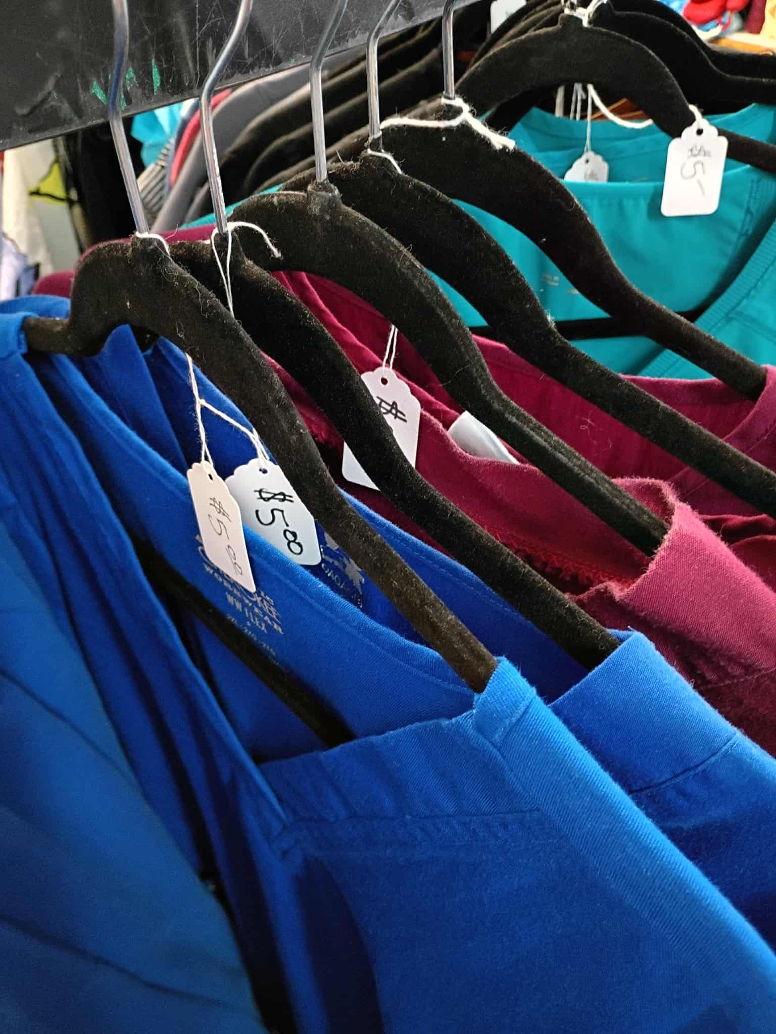 Clothes on black hangers, various colors: blue, burgundy, teal. Price tags are visible.