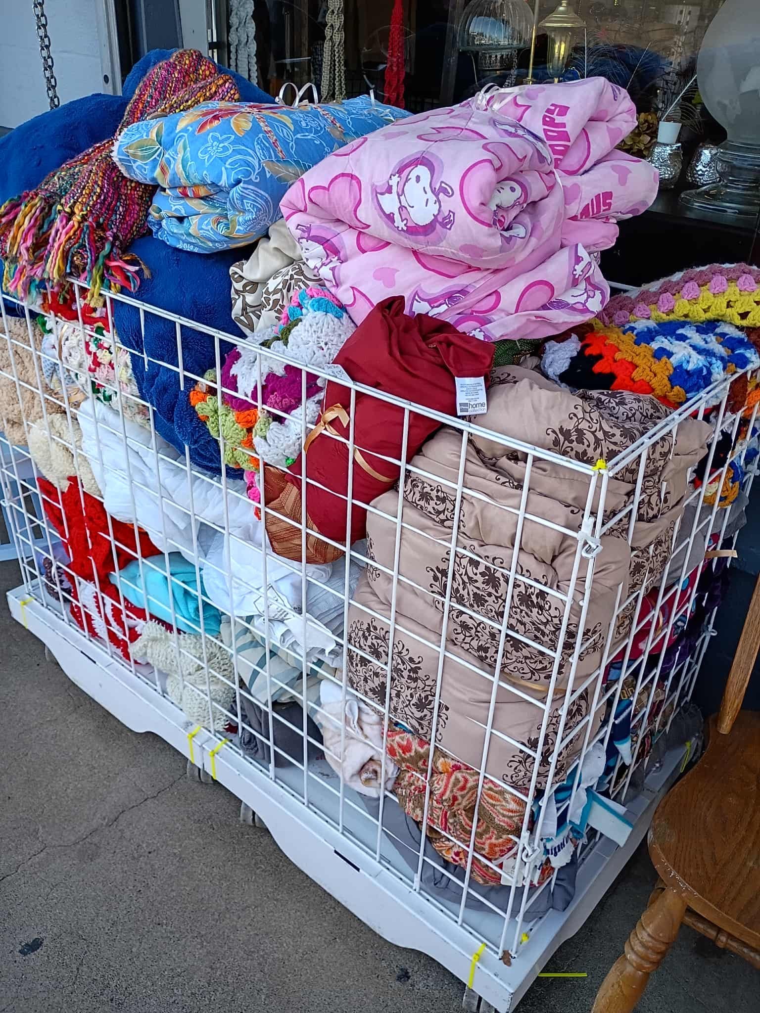 A white wire cage overflowing with folded blankets in various colors and patterns.
