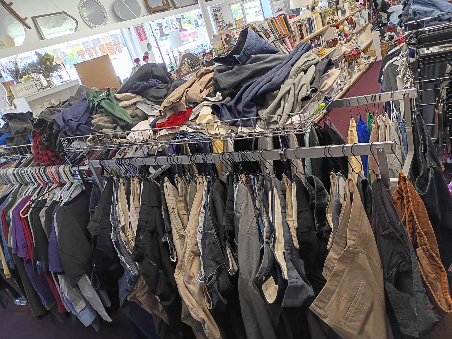 Clothing racks overflowing with pants and piles of clothes in a thrift store.