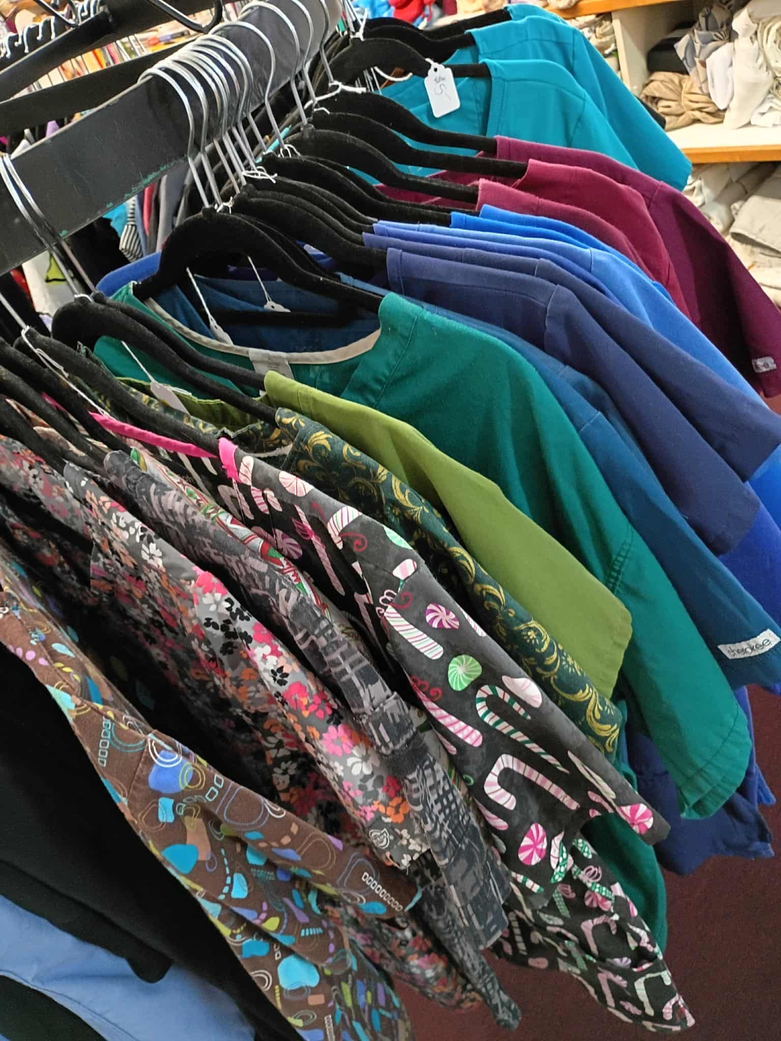 Clothing rack with colorful tops, including patterns and solid colors, hanging in a store.
