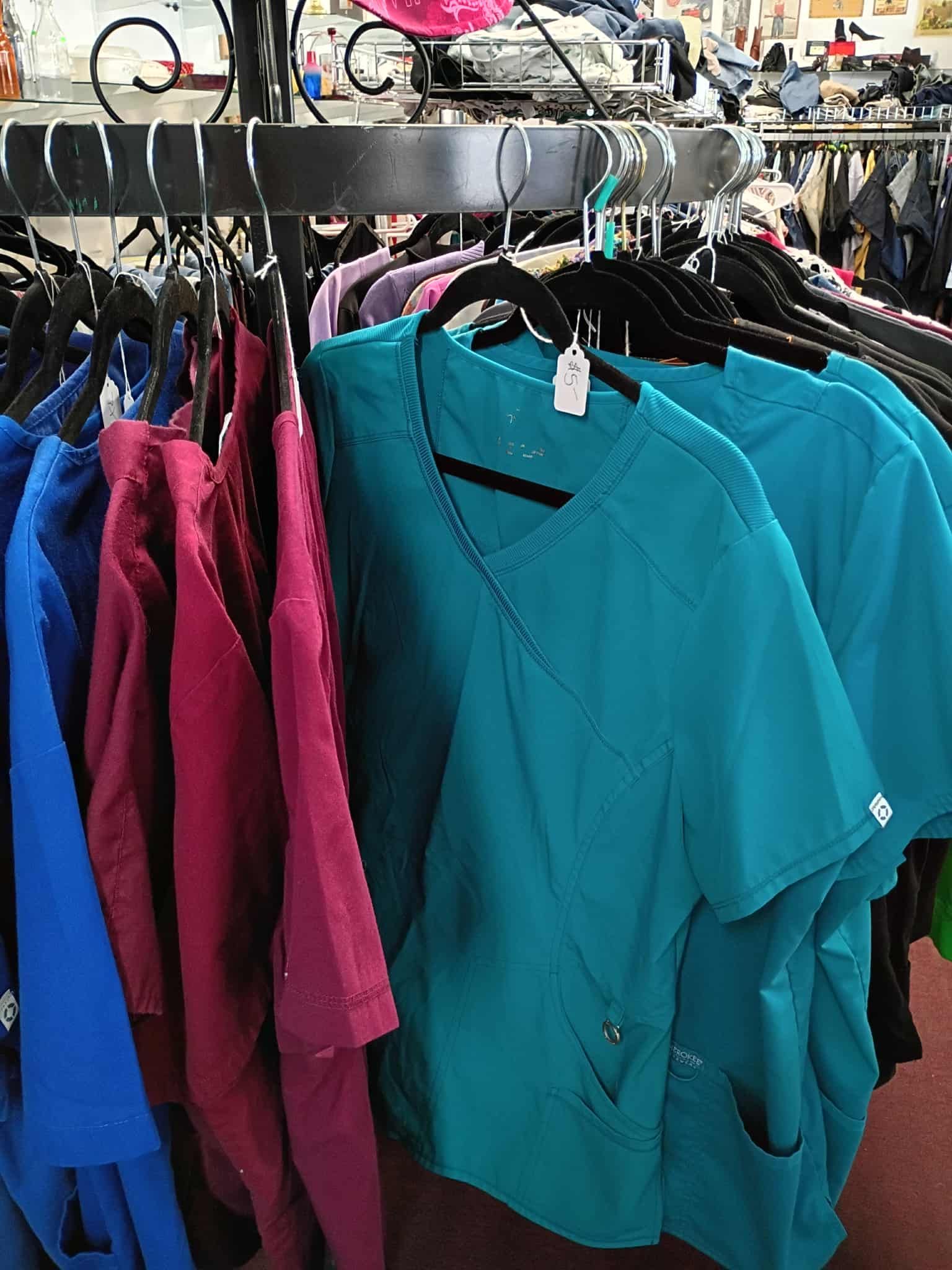 Rows of scrubs in various colors, teal, blue, and magenta, hang on clothing racks in a store.