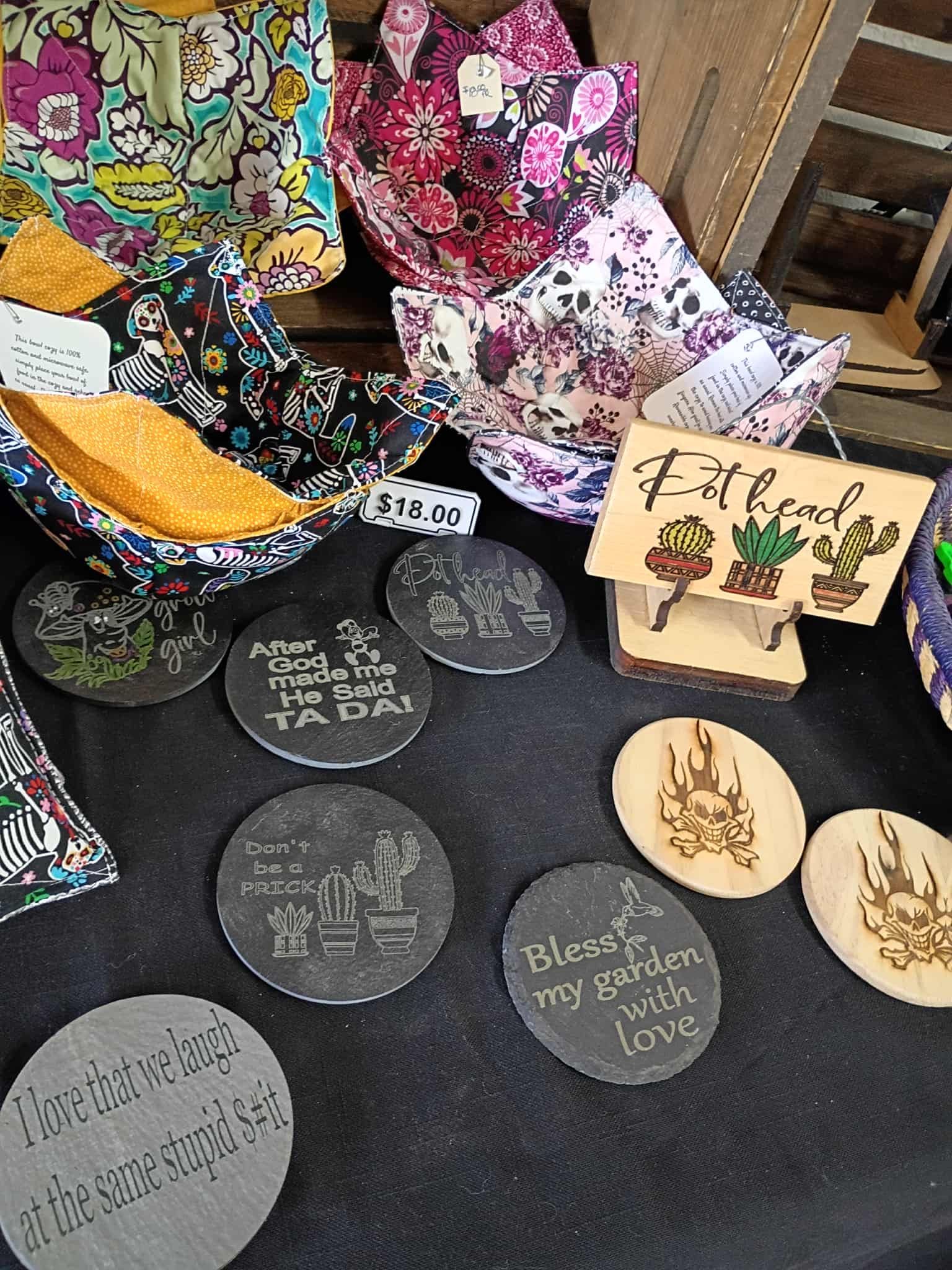 Handmade craft display: fabric bowl cozies, engraved coasters, and wood decor with garden themes.