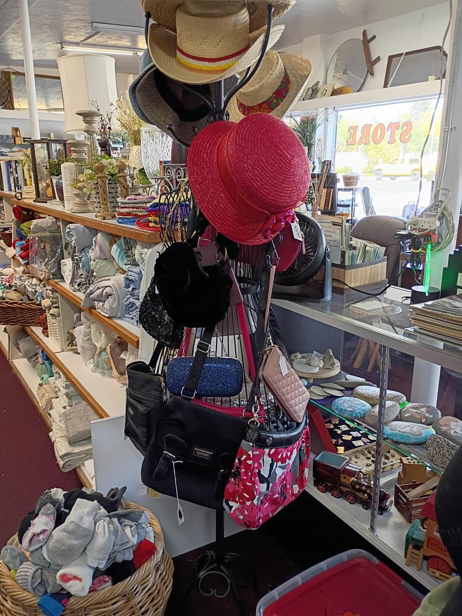 Inside a shop, a mannequin head adorned with hats and purses. Shelves filled with various items.