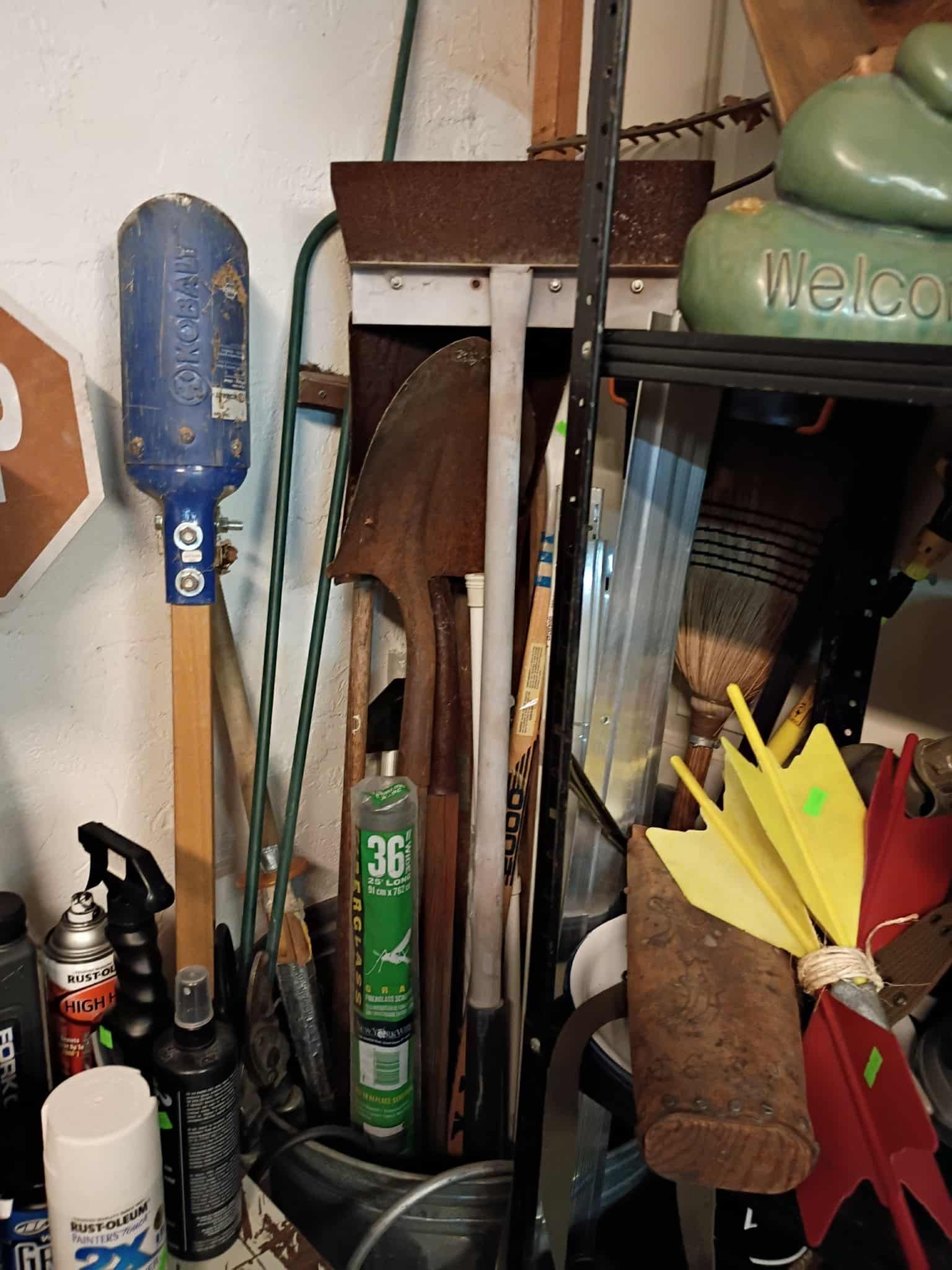 Assorted tools, including a shovel and axe, are stored in a cluttered garage.