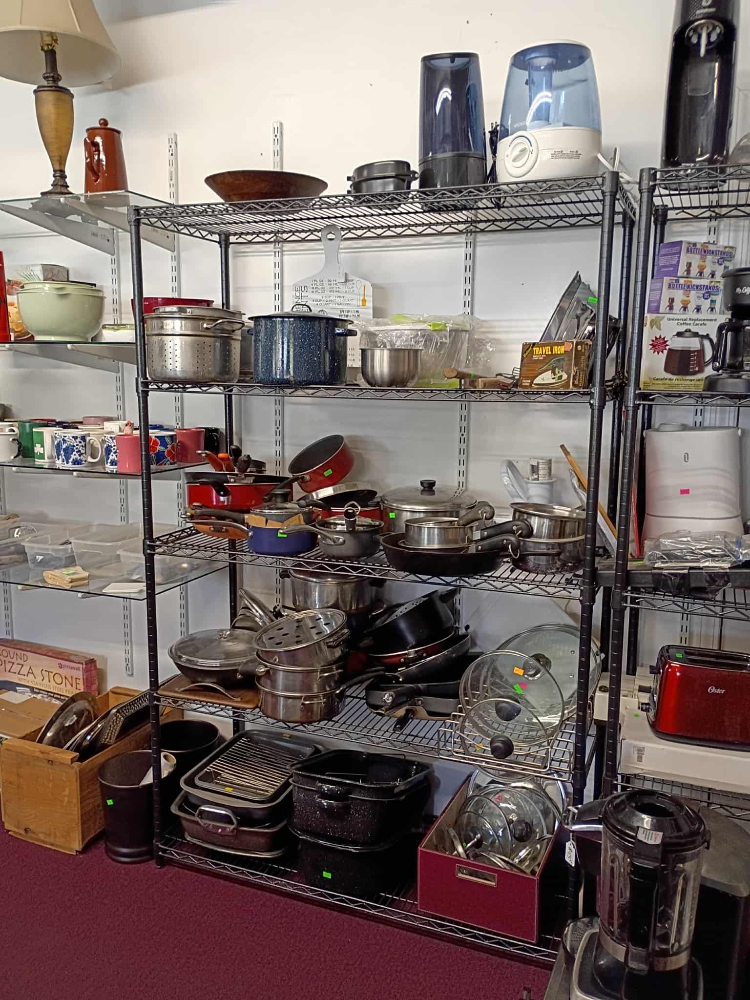 Shelves filled with kitchenware in a store, including pots, pans, appliances, and serving dishes.