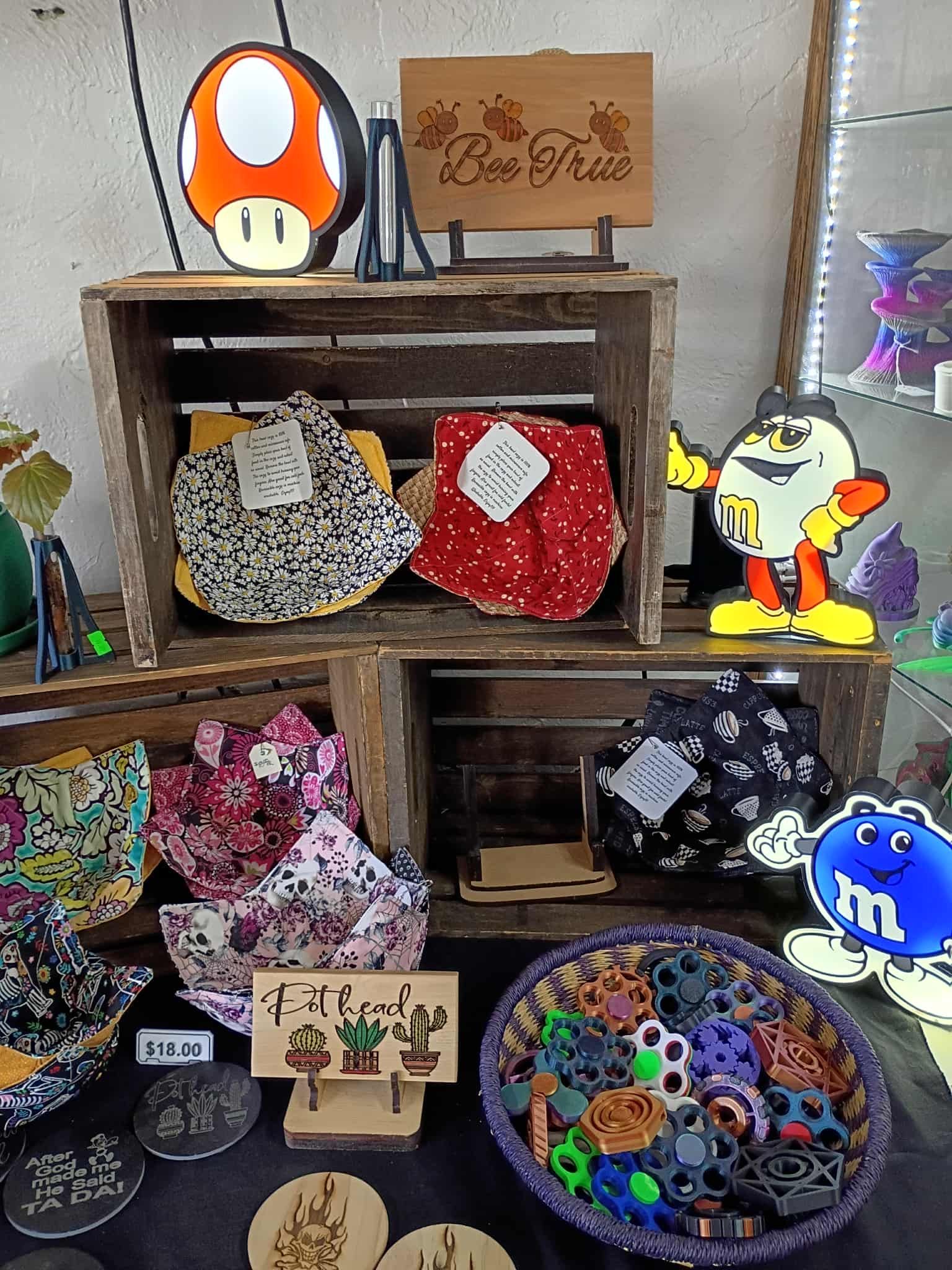 Display of handmade crafts including bowls, signs, and a Mario mushroom light, in a market setting.