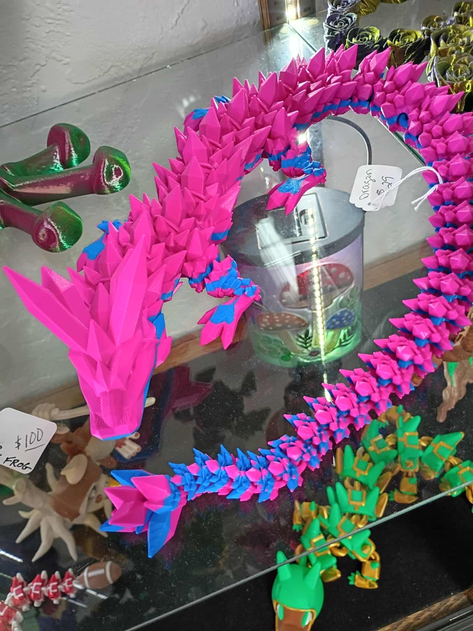 A vibrant pink and blue articulated dragon toy on display in a shop window.