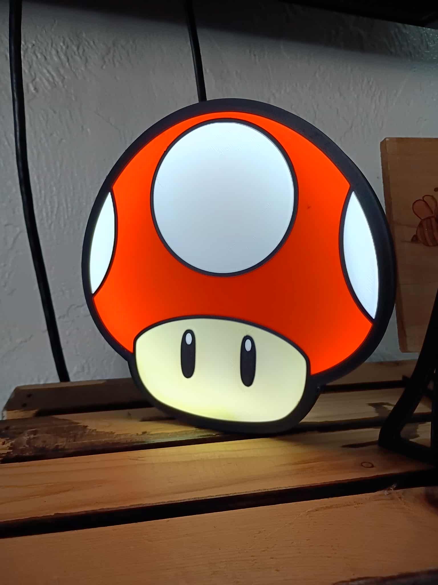 Lit-up Mario mushroom lamp on a wooden shelf. Red, white, and orange colors.