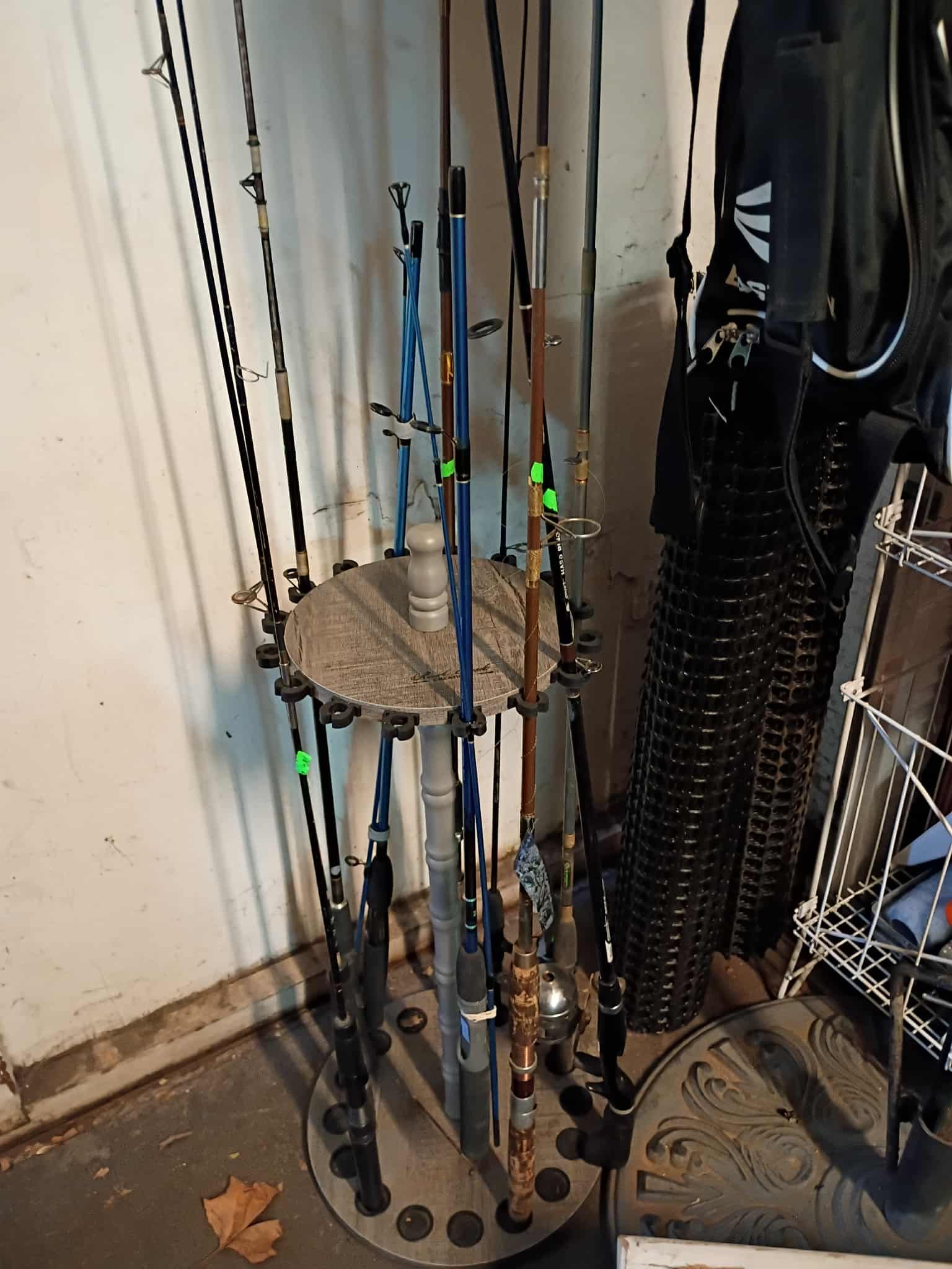 Fishing rods in a metal stand, indoors, near a wall and other items.