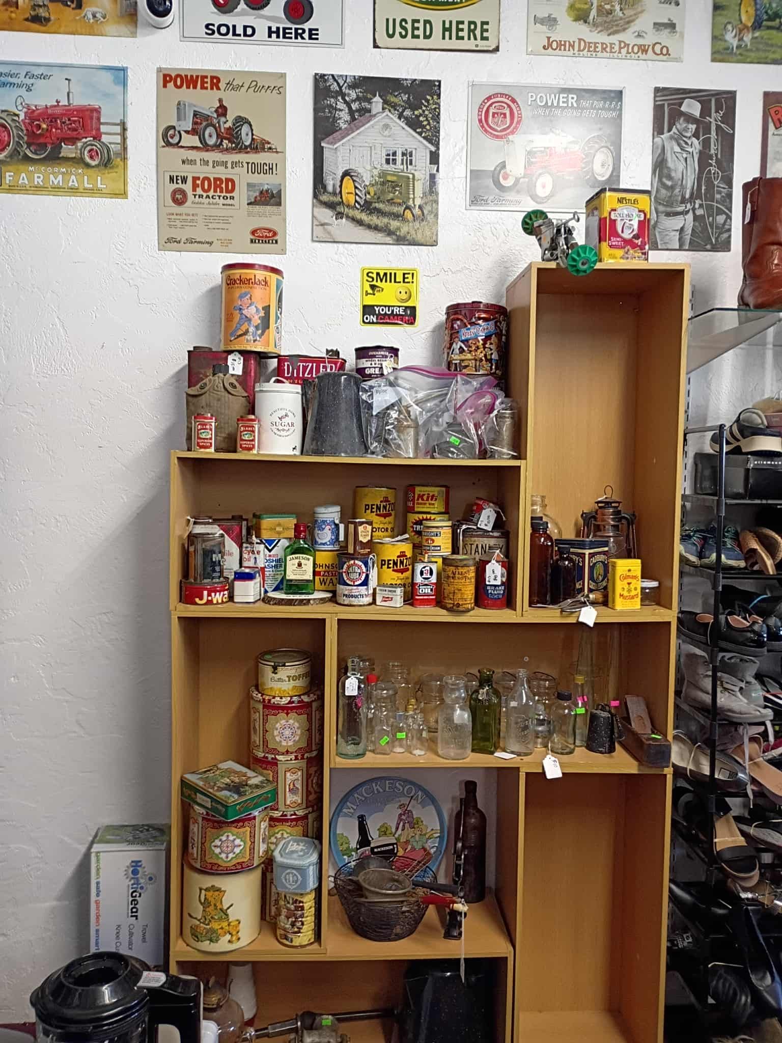 A wooden shelf filled with vintage jars, tins, and collectibles in a cluttered shop.