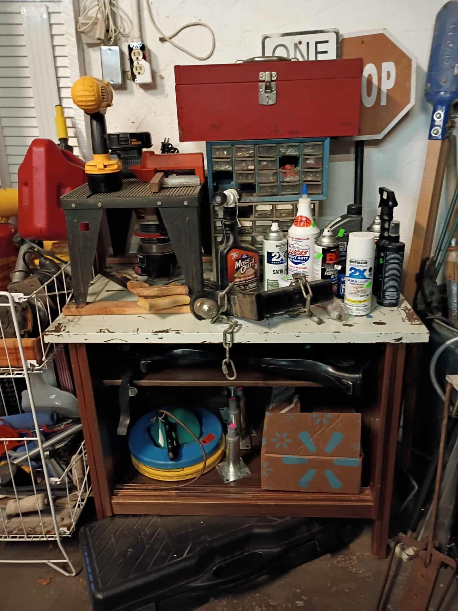 Workshop table with tools, toolbox, spray cans, and metal shelving.