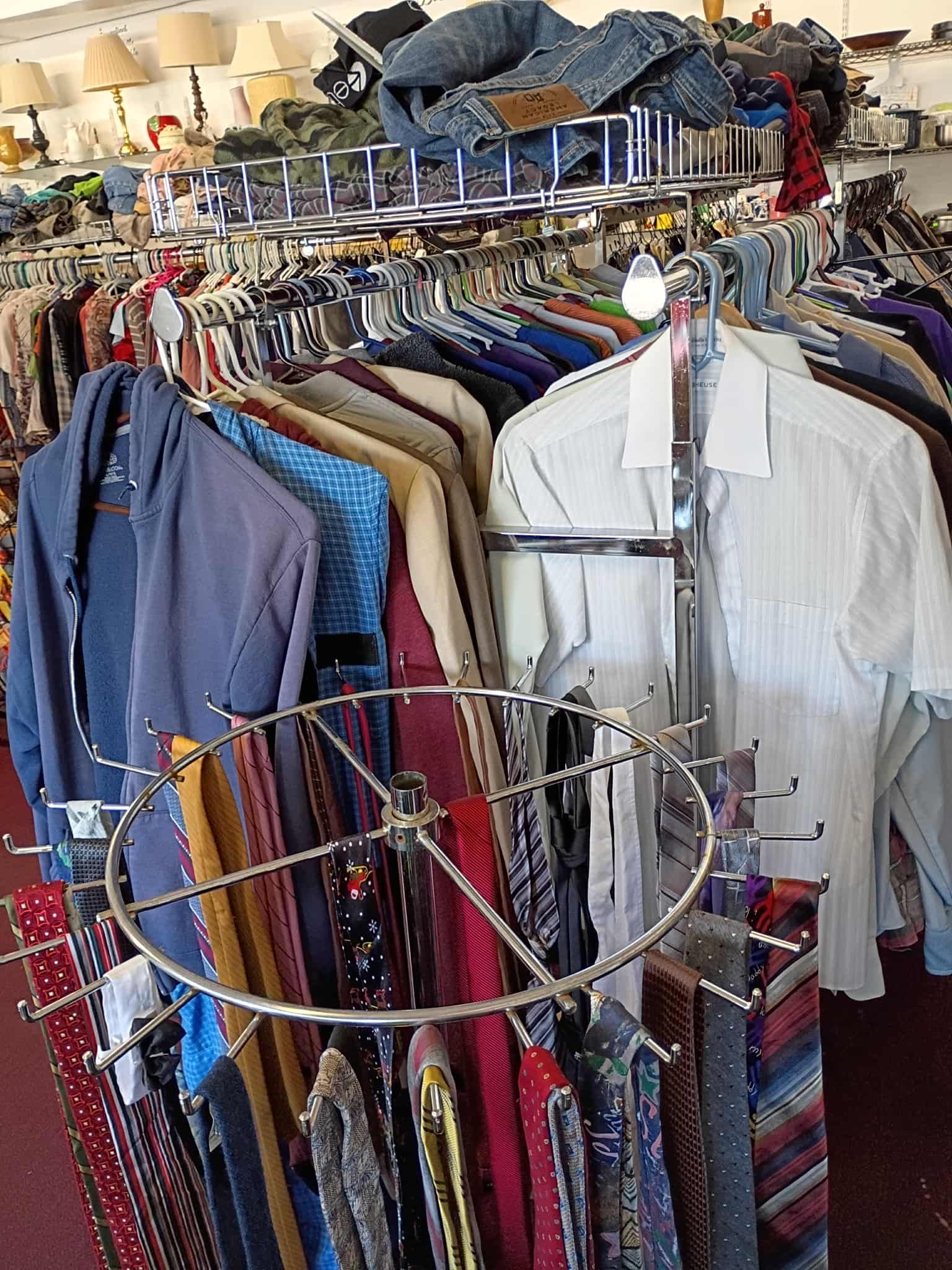 Clothing racks filled with various apparel at a retail store. Ties displayed in foreground, shirts and jackets behind.