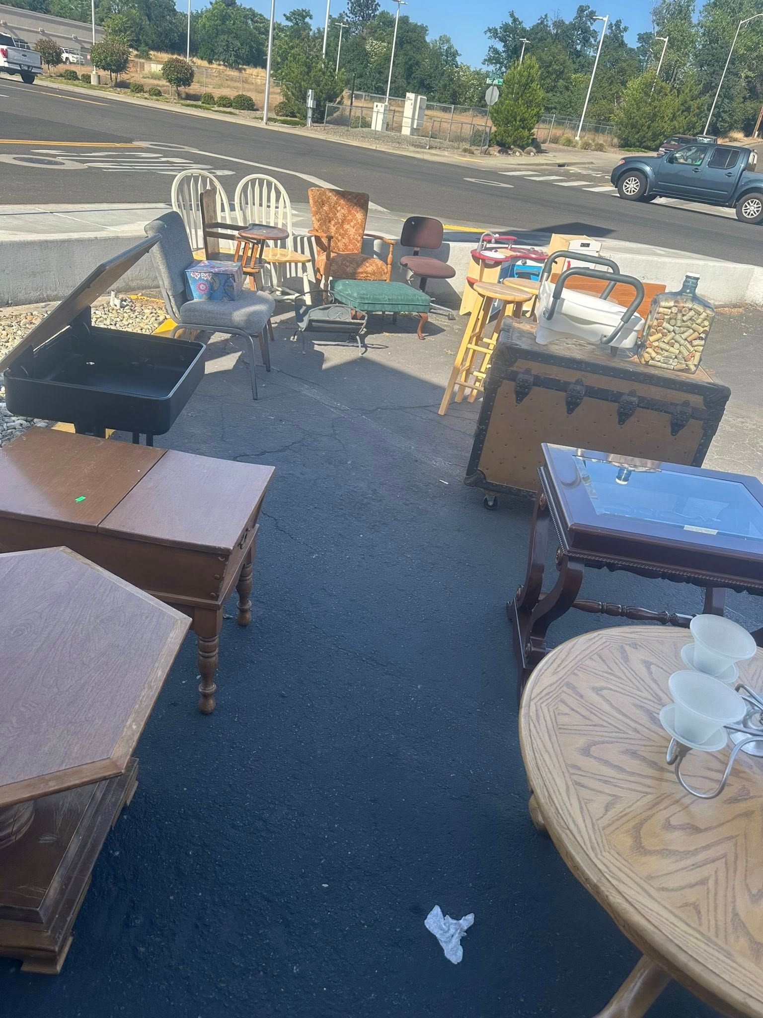 Furniture for sale displayed on an asphalt surface near a parking lot.