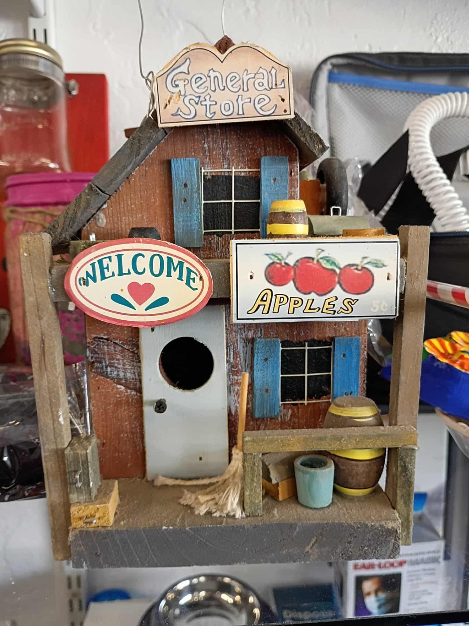 Birdhouse shaped like a general store with a welcome sign and apple sign.