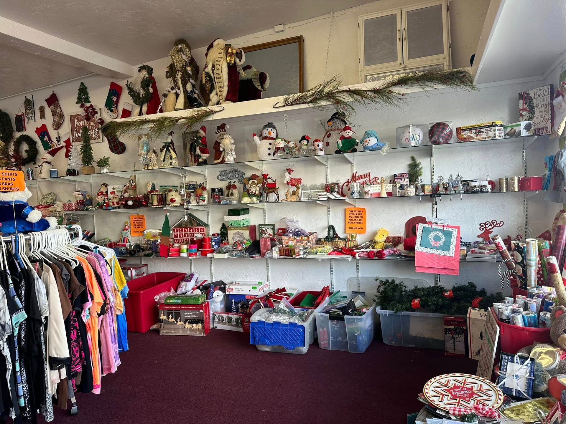 A thrift store interior with clothes racks and shelves displaying holiday decorations and other items.