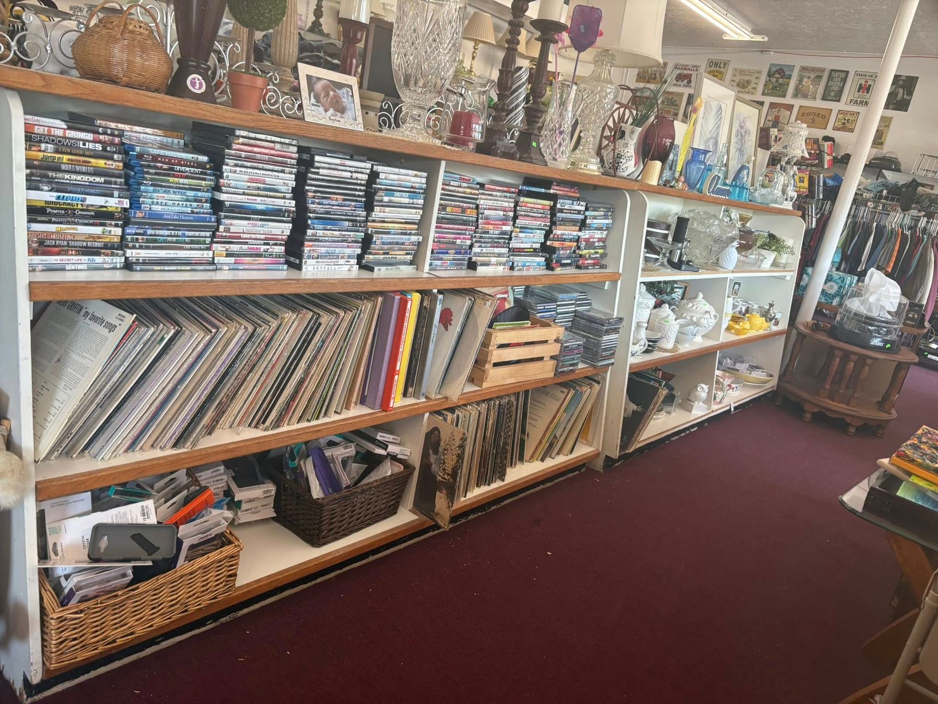 Shelves in a thrift store display DVDs and vinyl records; items on top shelves. Red carpet.