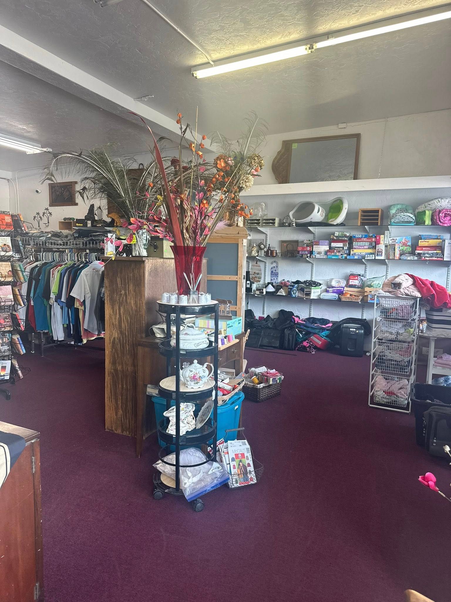 A brightly lit shop interior with various merchandise on shelves and racks. Dark red carpet.