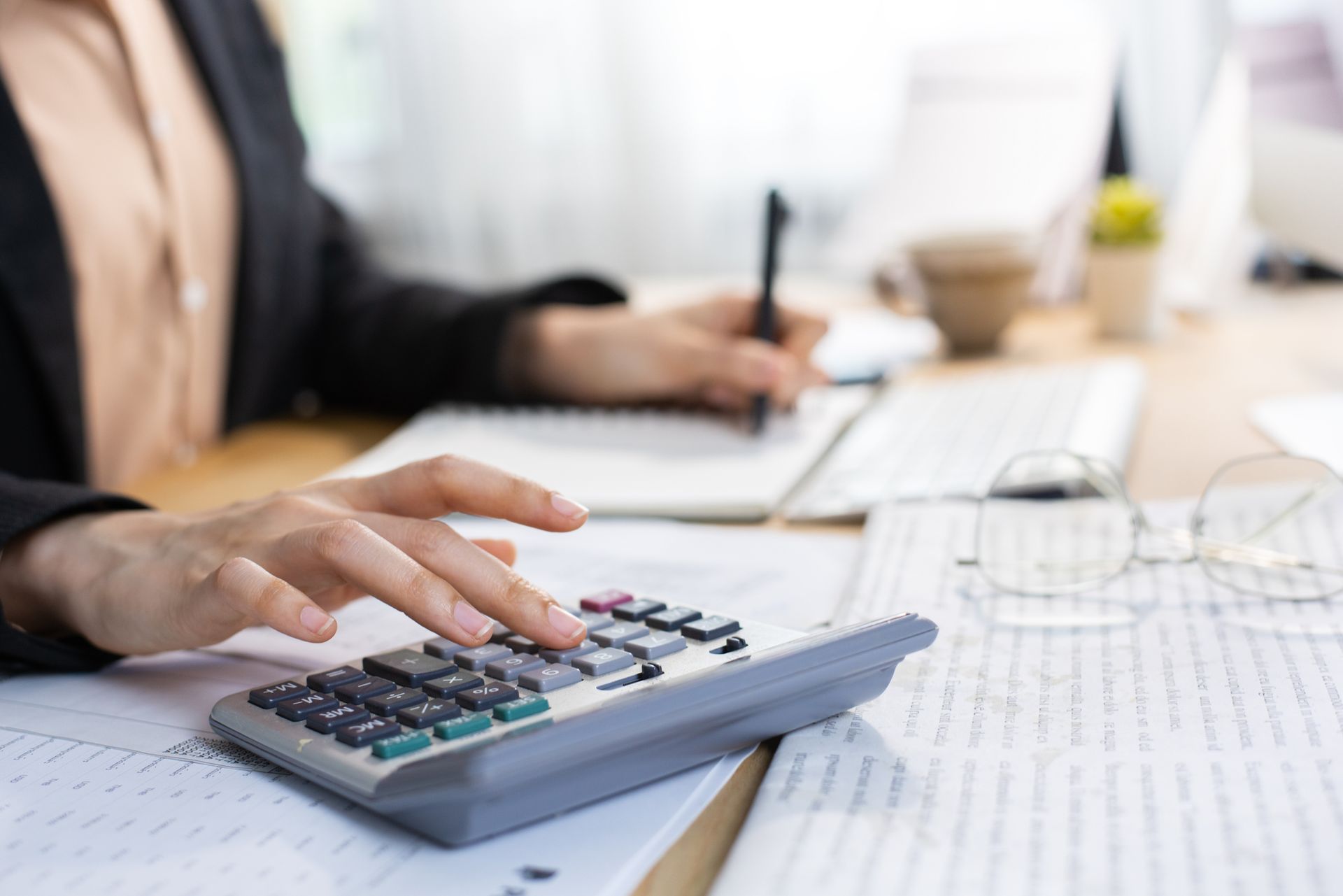 Person using a calculator and writing notes at a desk with papers
